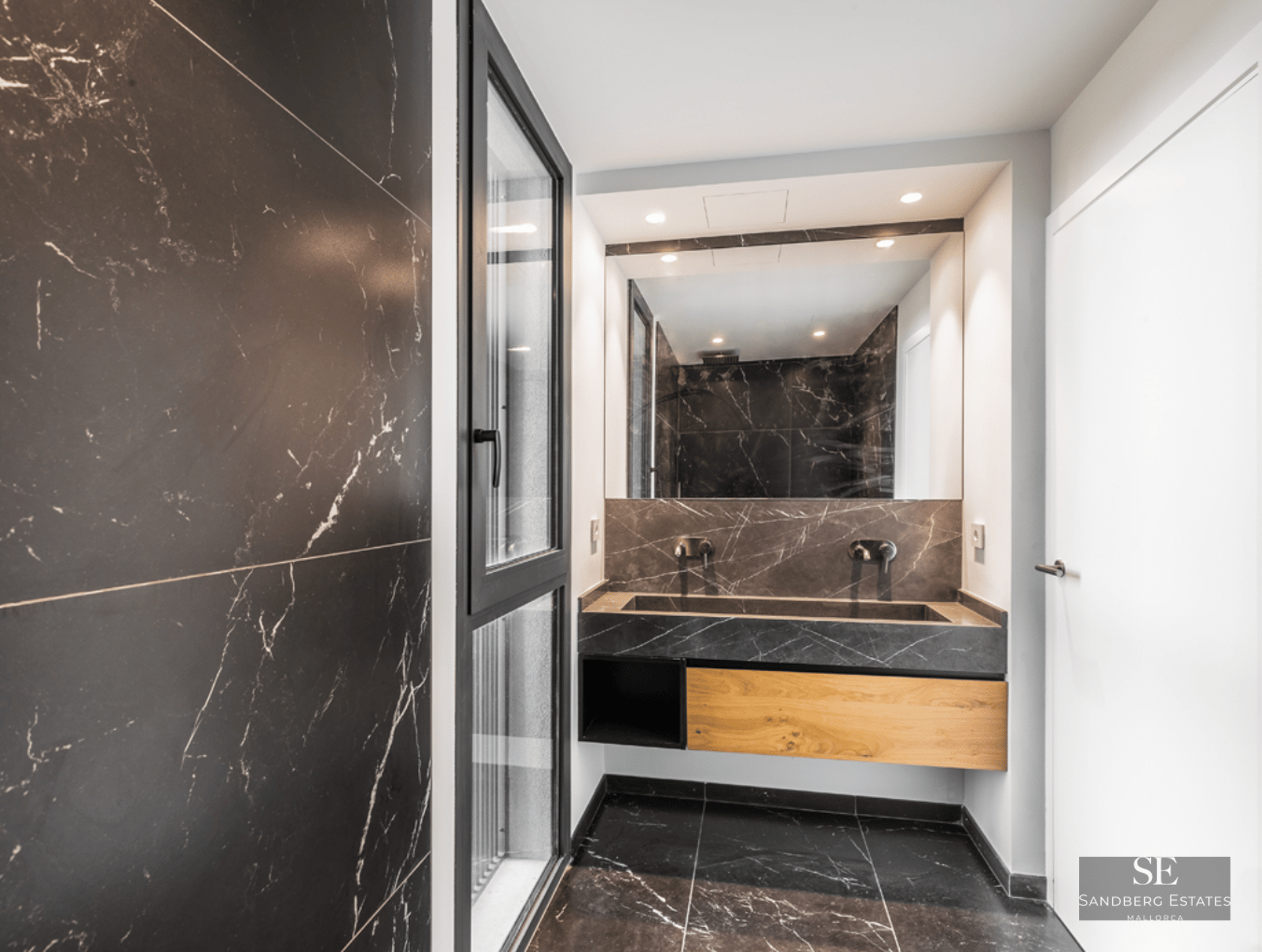 Modern bathroom with black marble walls and floor, an integrated stone sink, and a large mirror.