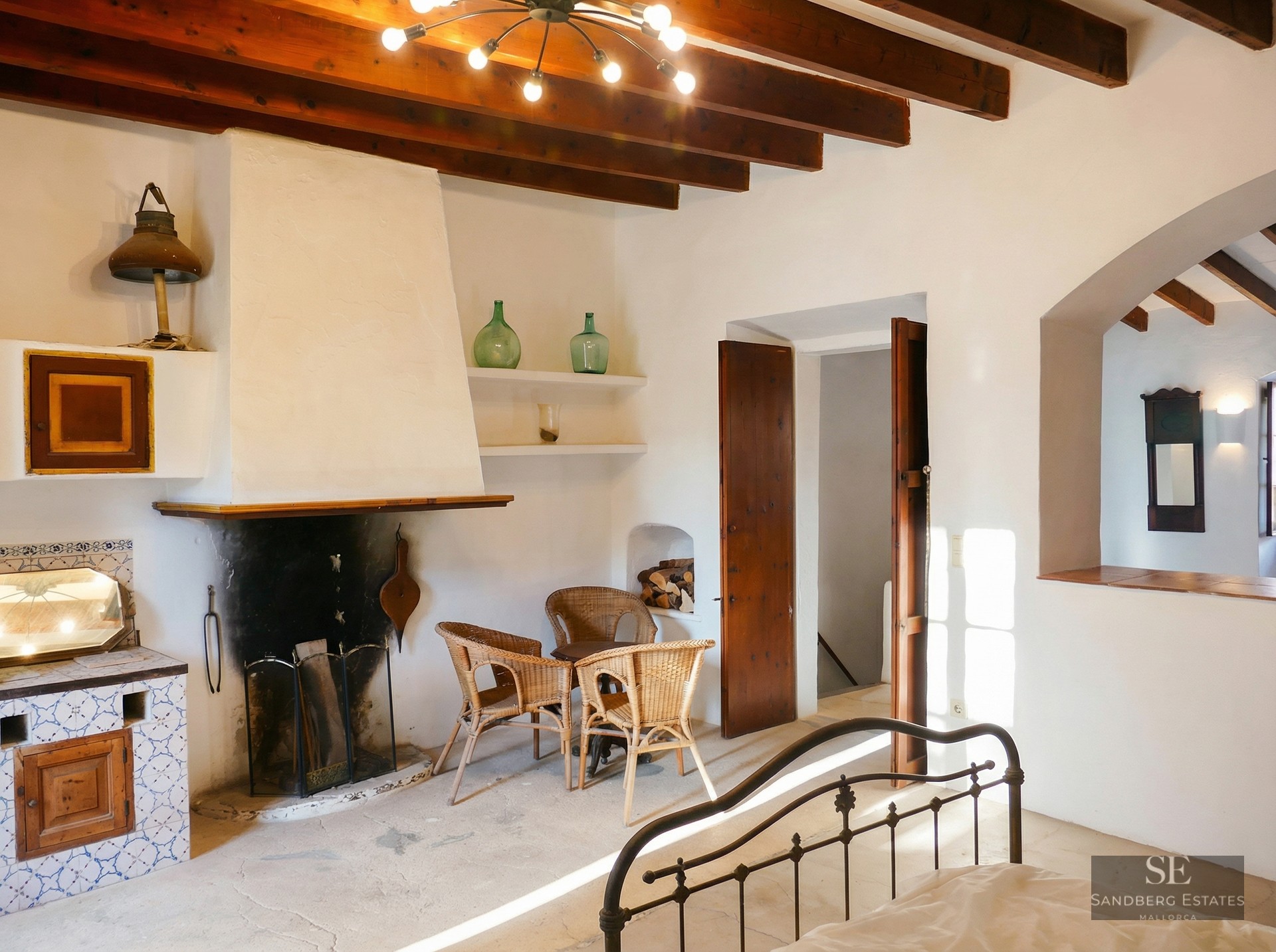 Master bedroom featuring exposed wood beams, a large white fireplace, and rustic wicker seating.