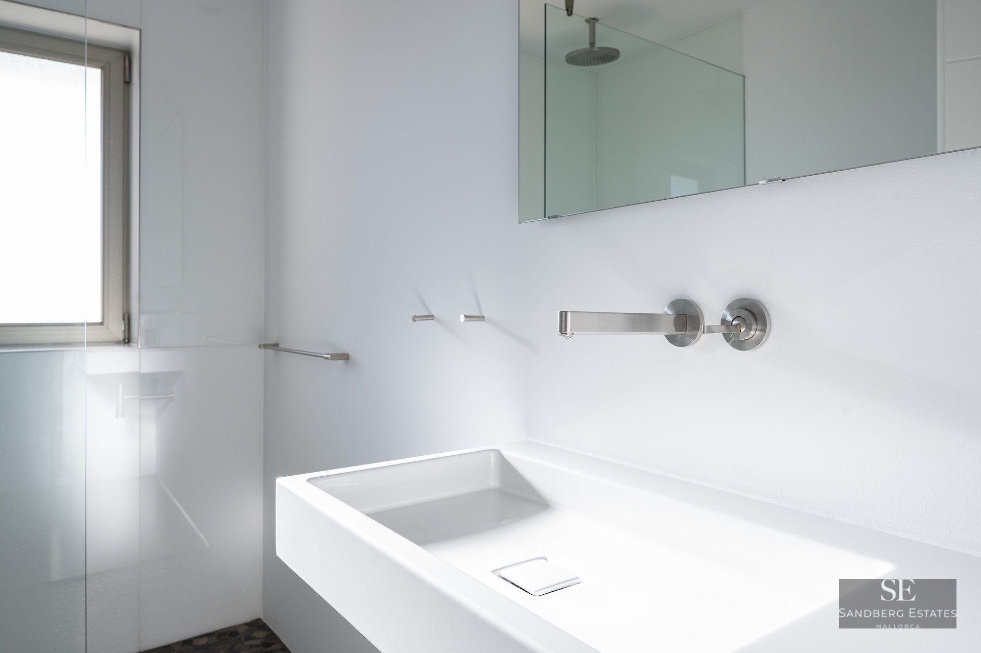 White rectangular sink with wall-mounted chrome faucet in a bright, modern bathroom.