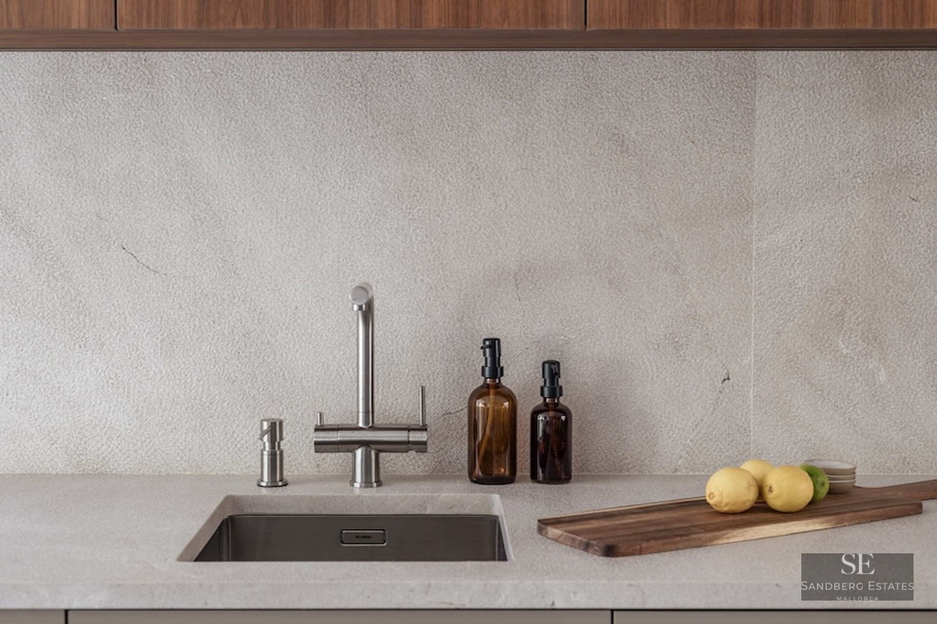 Close-up of a kitchen sink with a stainless steel faucet, stone countertop, and wooden cutting board.