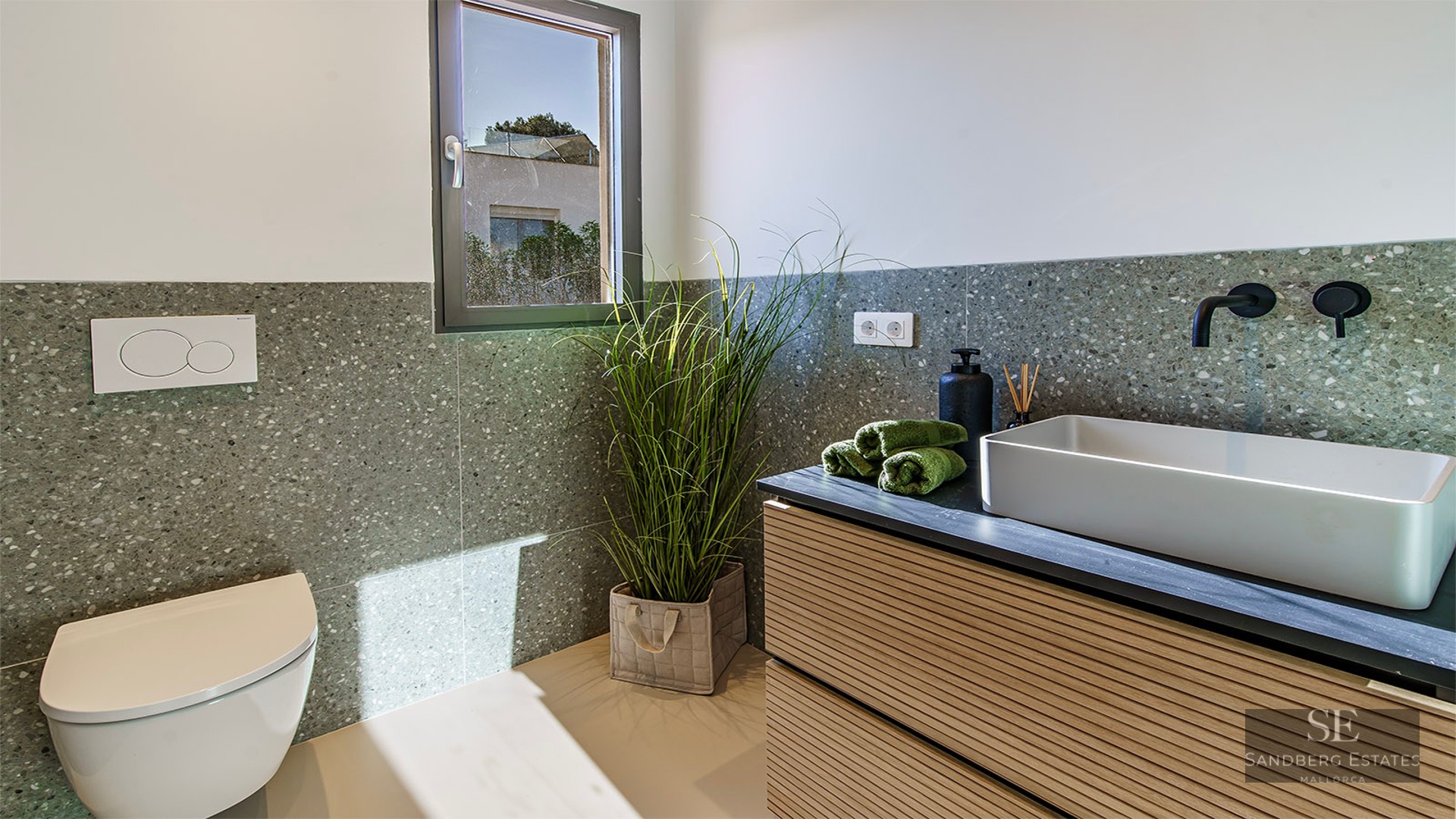 Minimalist bathroom featuring a vessel sink, black faucet, wall-hung toilet, and green terrazzo walls.