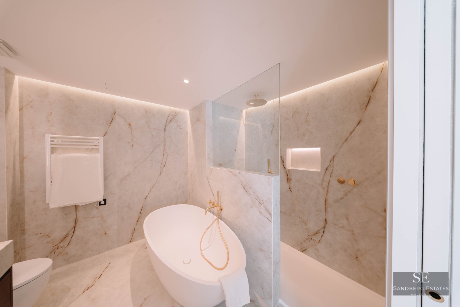 Elegant bathroom featuring a freestanding oval tub, glass shower, and marble walls with gold fixtures.