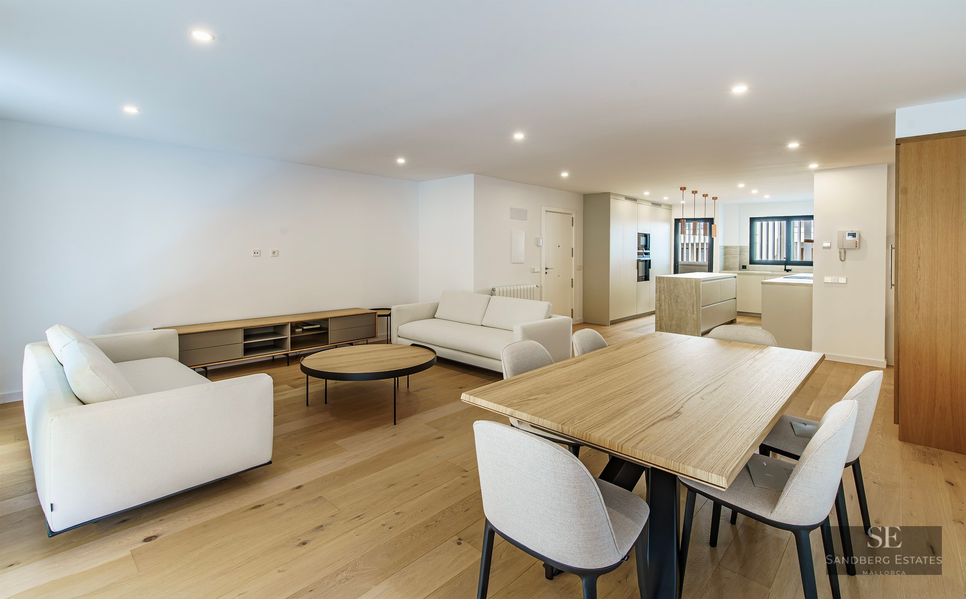 Pièce moderne spacieuse avec canapés blancs, grande table à manger en bois et cuisine contemporaine en arrière-plan.