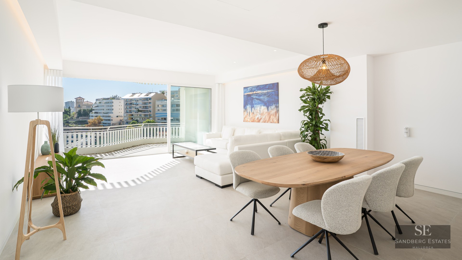 Bright open-plan living and dining room with wooden furniture, white sofa, and terrace access with city views.