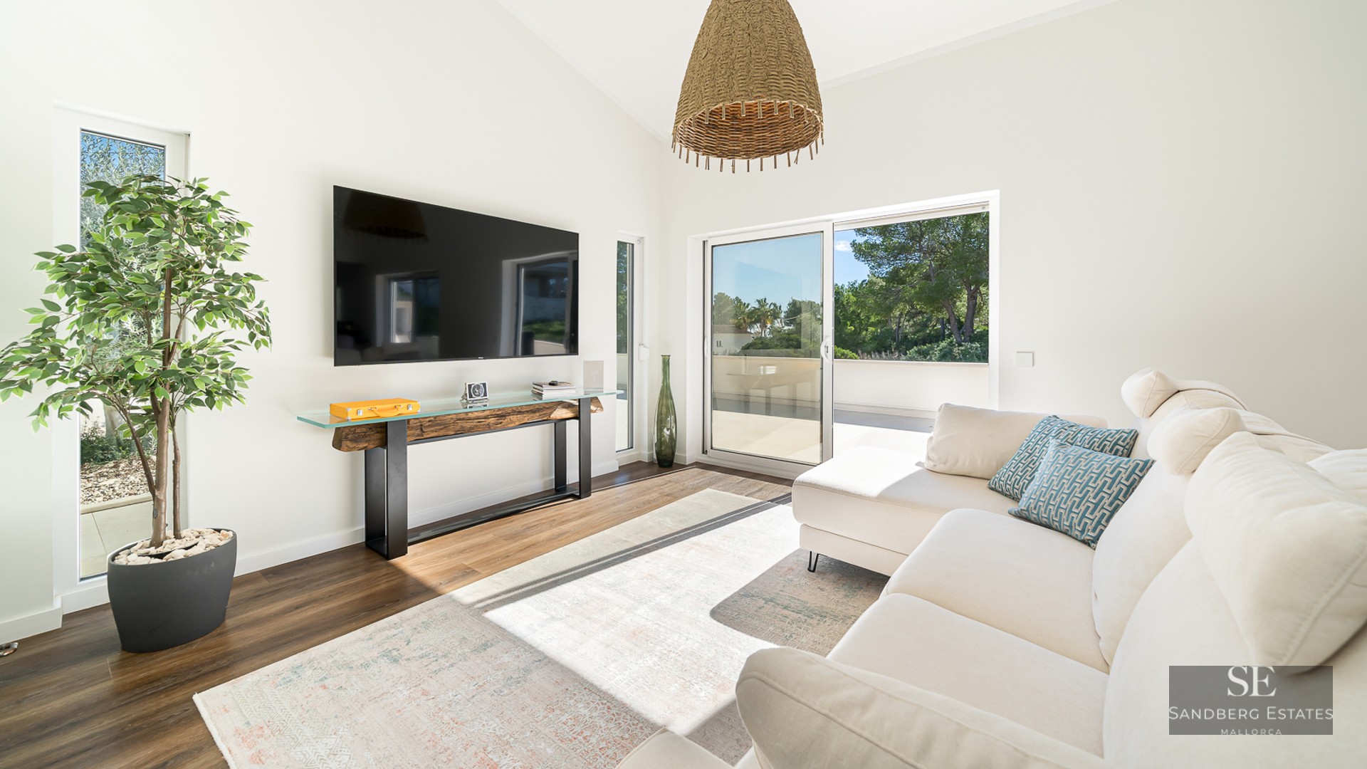 Salon moderne avec canapé d'angle blanc, TV murale, console rustique et grandes baies vitrées coulissantes.