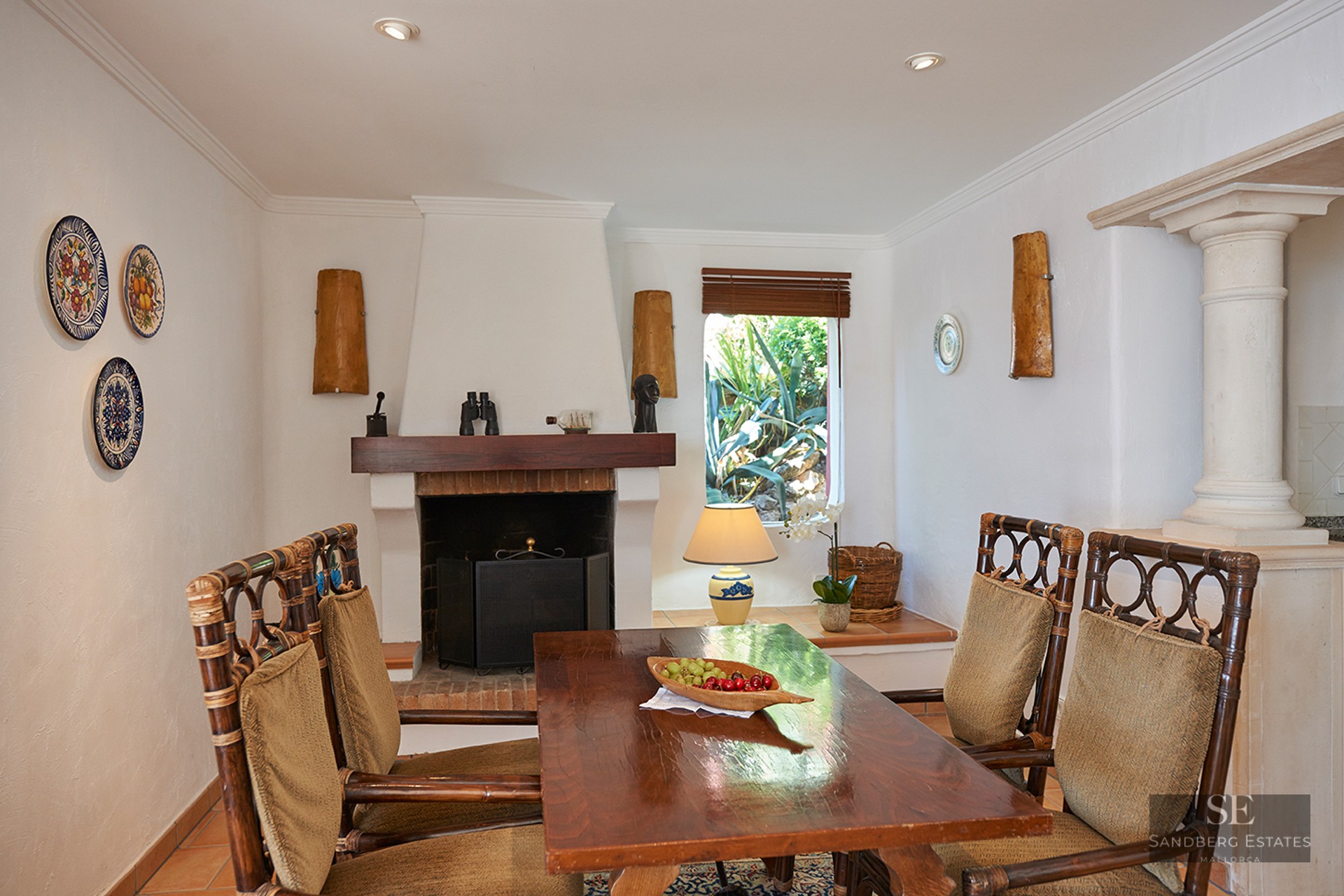 A dining room featuring a wooden table, bamboo chairs, a white fireplace, and decorative wall plates.