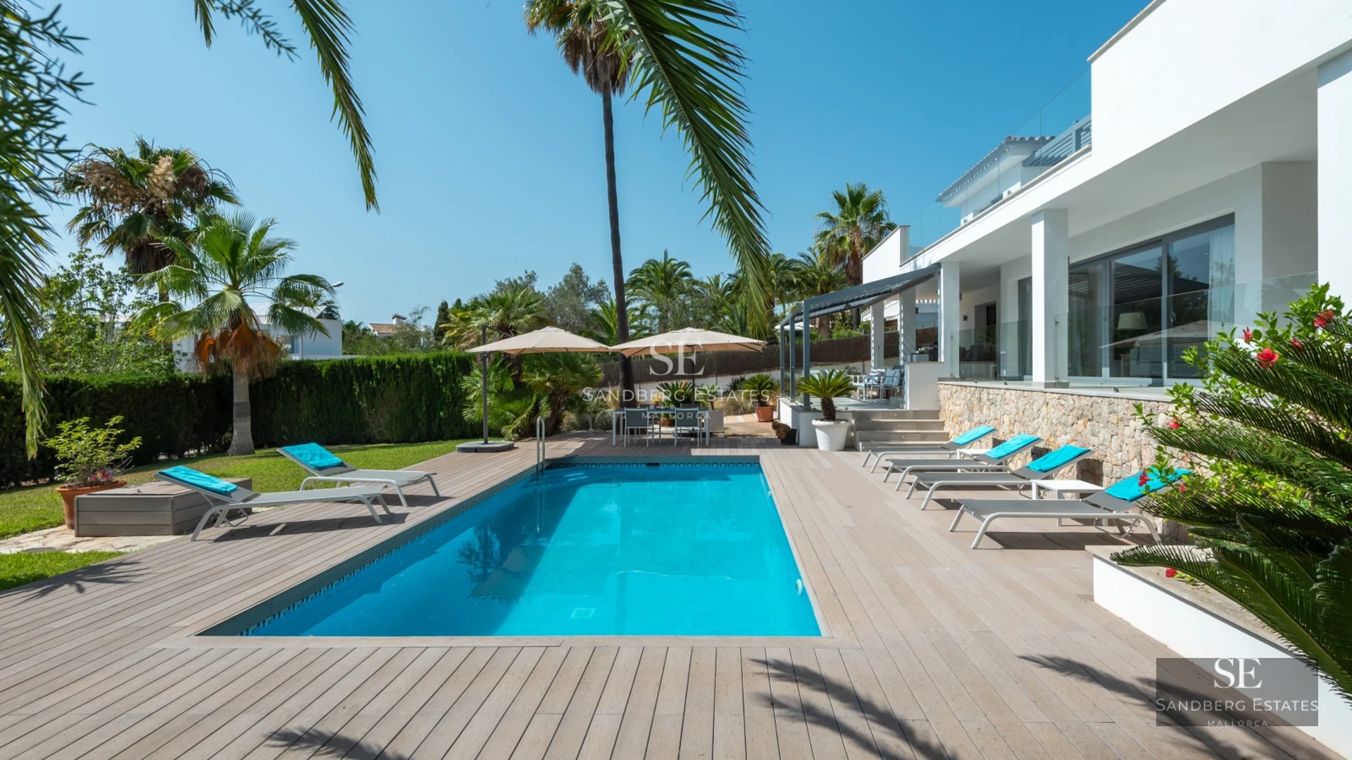 Wide view of bright living room with infinity pool and modern furniture. Large windows and lush garden.