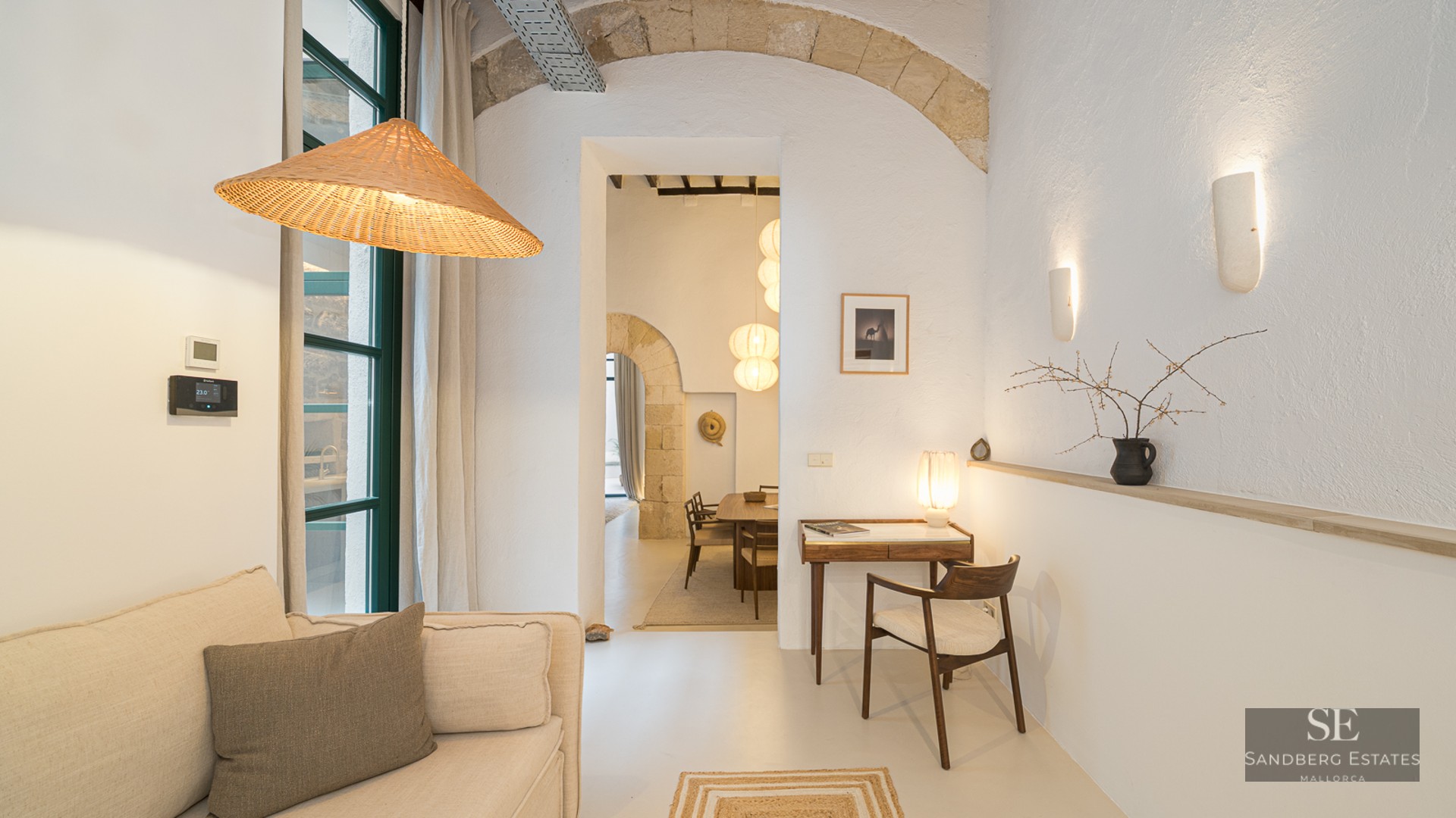 Modern living room with a beige sofa, stone archway, and a small desk leading to a dining area.