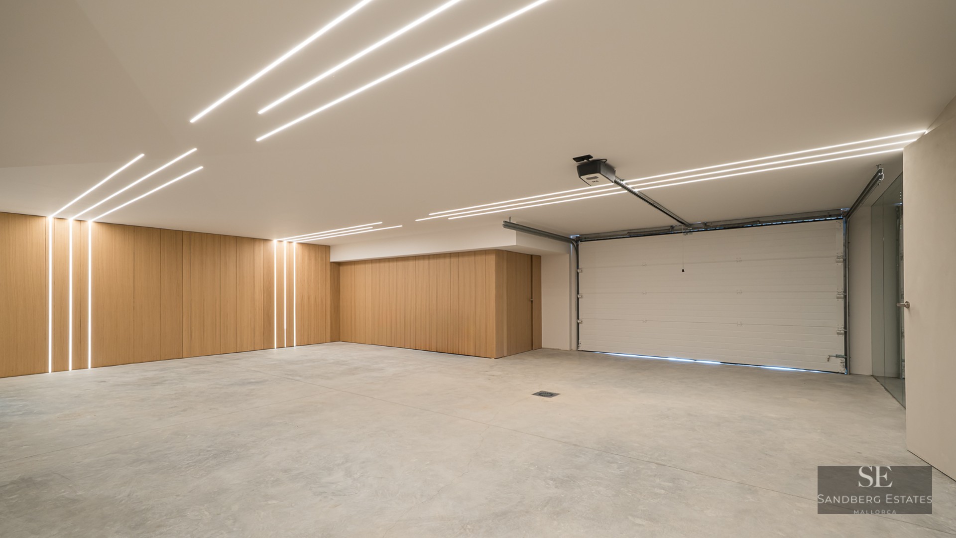 Spacious modern garage with concrete floor, wood wall panels, and linear LED light strips on the ceiling.