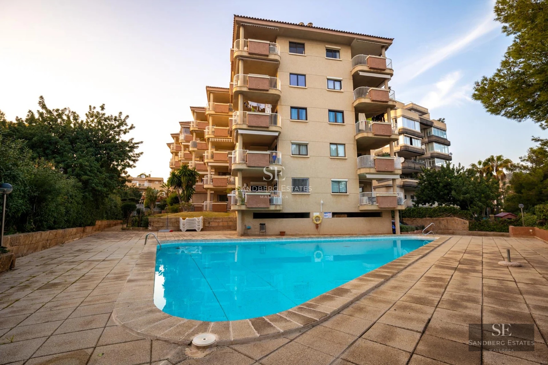 Vue de la piscine à débordement avec des chaises longues, entourée de pelouse et d'une villa moderne avec de grandes baies vitrées. Paysage luxuriant en arrière-plan.