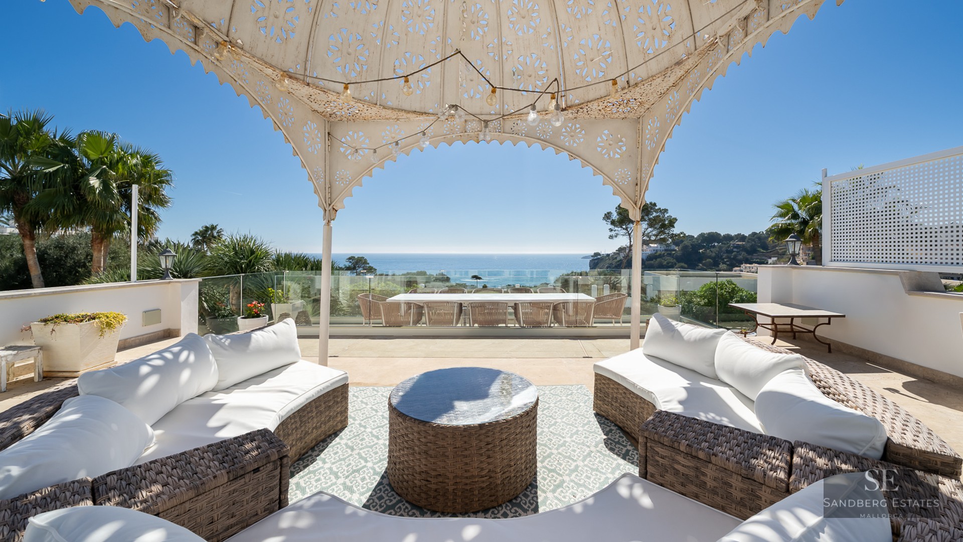 Spacious terrace with wicker sofas under a decorative gazebo overlooking the Mediterranean sea.