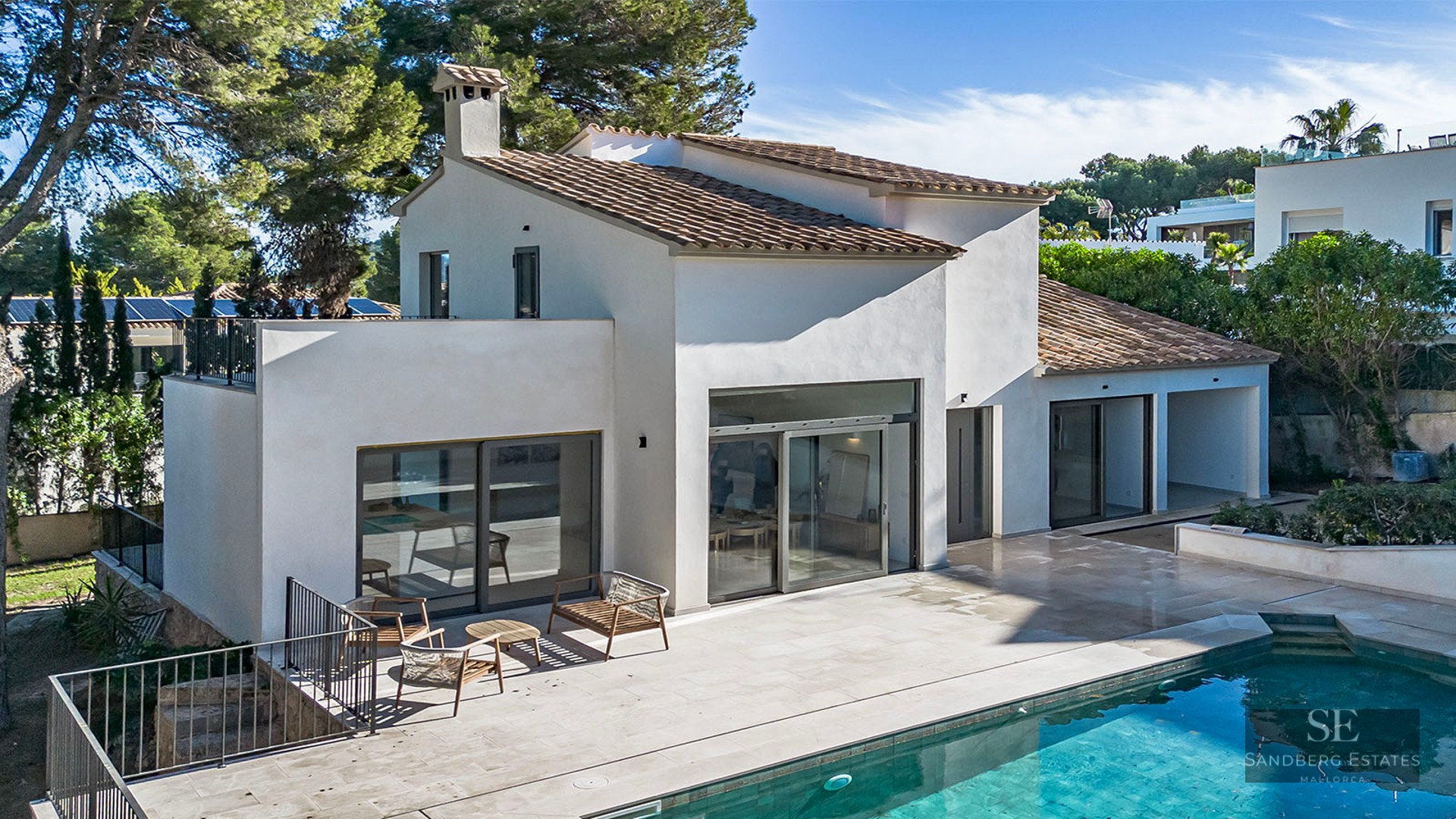 Modern white villa with a terracotta roof, large glass doors, and a stone terrace next to a turquoise swimming pool.