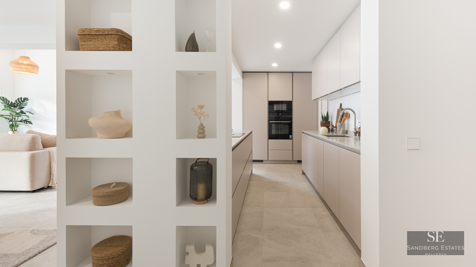 Modern galley kitchen with taupe cabinets next to a white partition wall with eight decorative recessed niches.