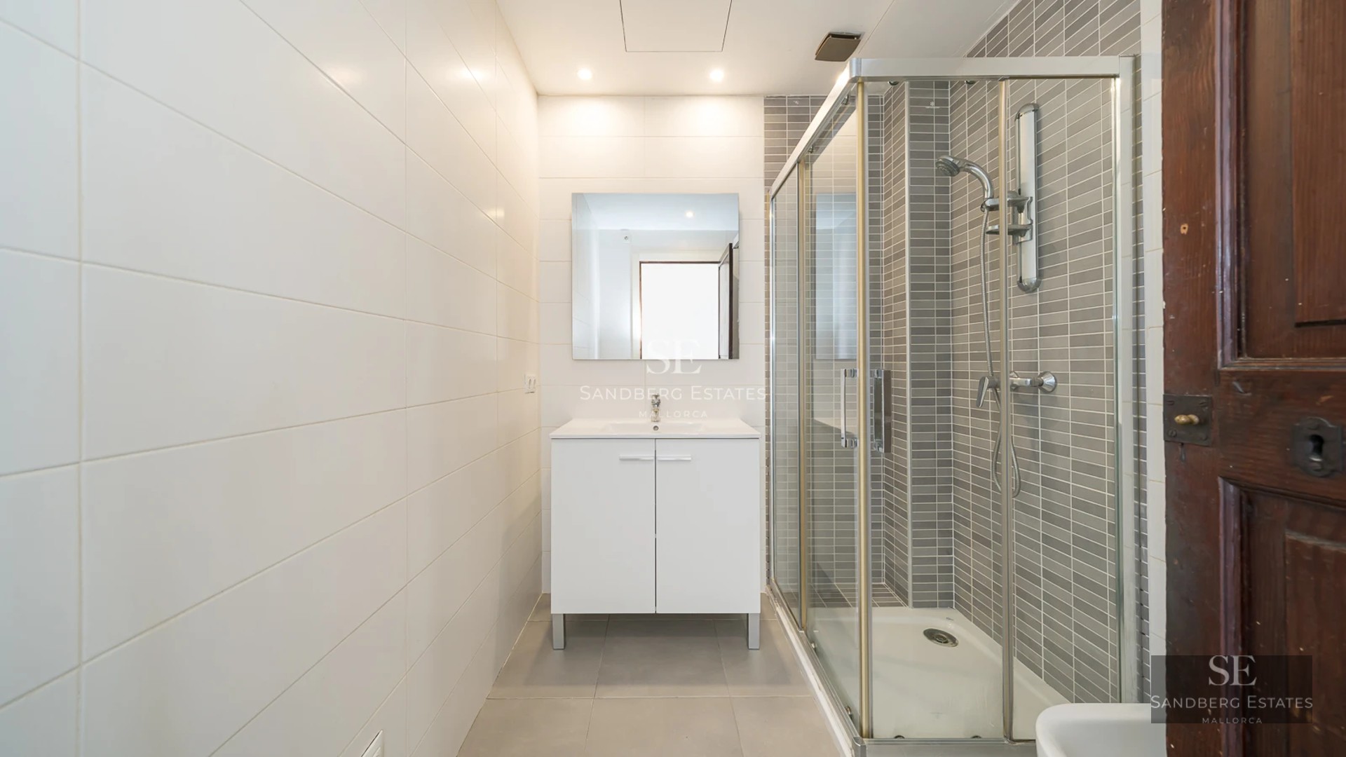 Spacious balcony with sea view. Glass railing, tiled floor, modern outdoor furniture. Blue sky, calm sea.