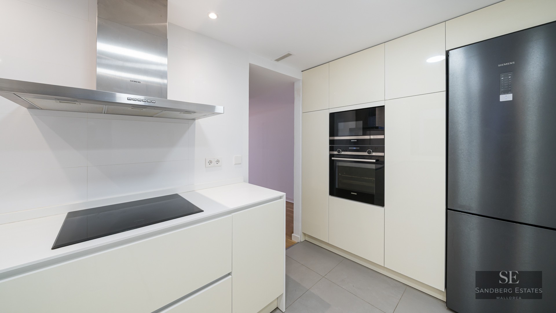 Minimalist white kitchen featuring a stainless steel hood, built-in oven, and a modern black refrigerator.