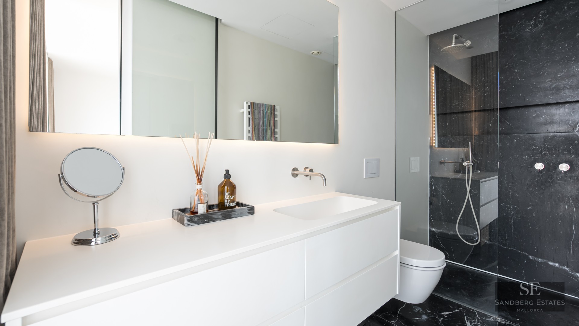 Minimalist white bathroom featuring a floating vanity and a walk-in shower with luxurious black marble walls.