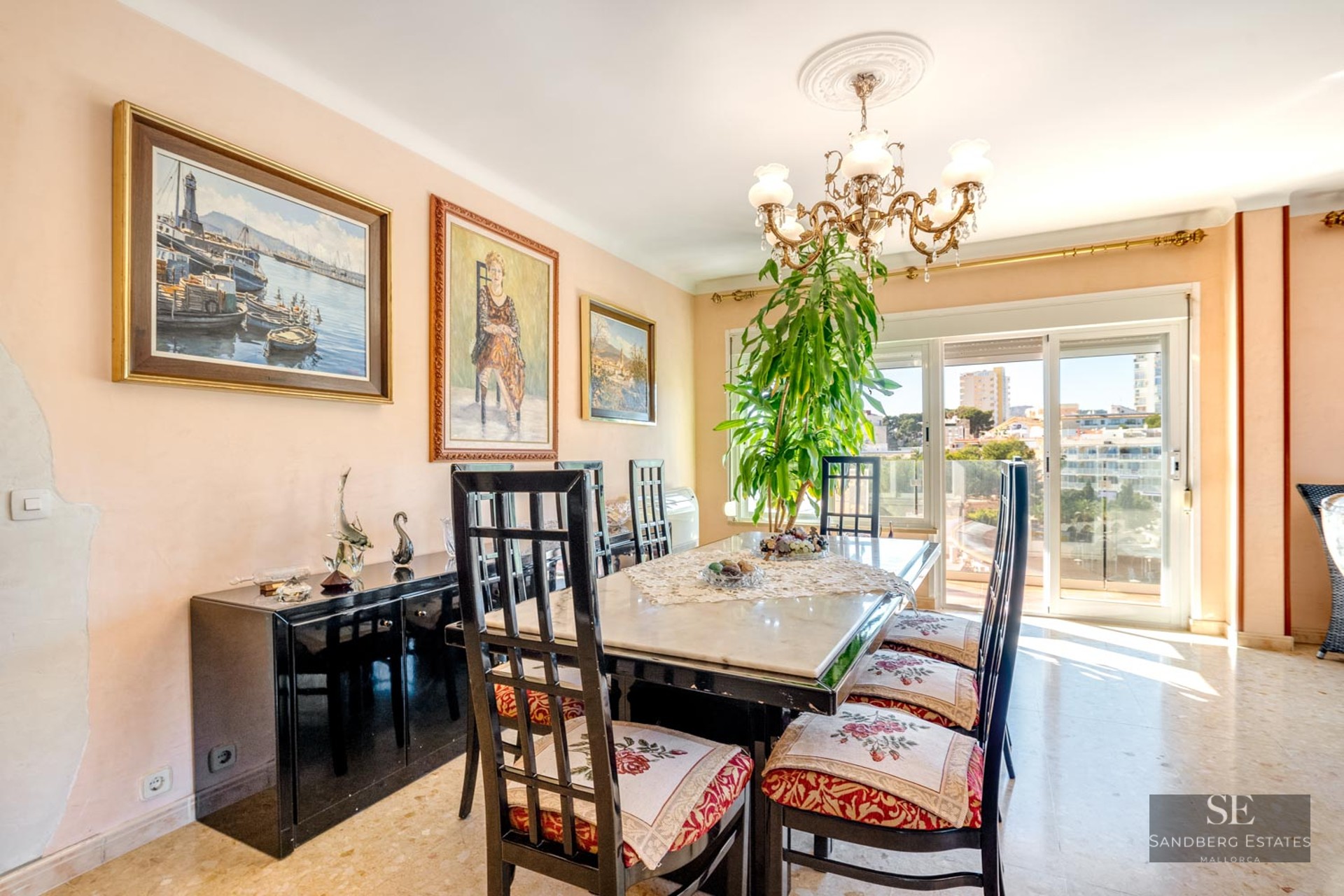 Traditional dining room with a marble table, high-backed chairs, a chandelier, and large glass doors with a city view.