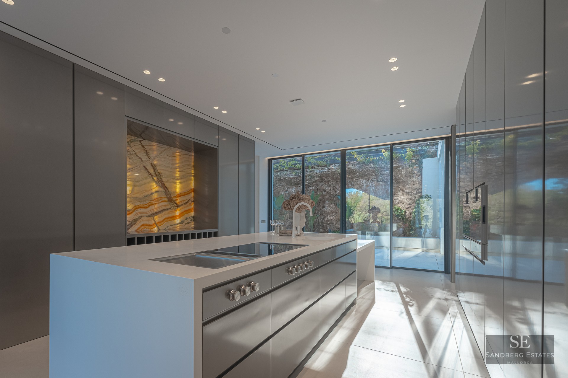 Modern minimalist kitchen with large island, sleek grey cabinetry, and a stunning backlit golden marble feature wall.