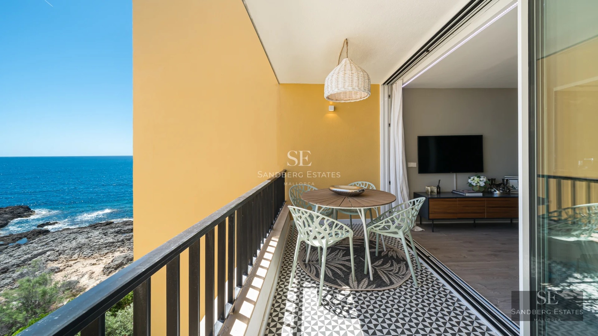 Bright living room with large windows and balcony overlooking the sea. Modern design, light wood floors, and minimalist furniture.