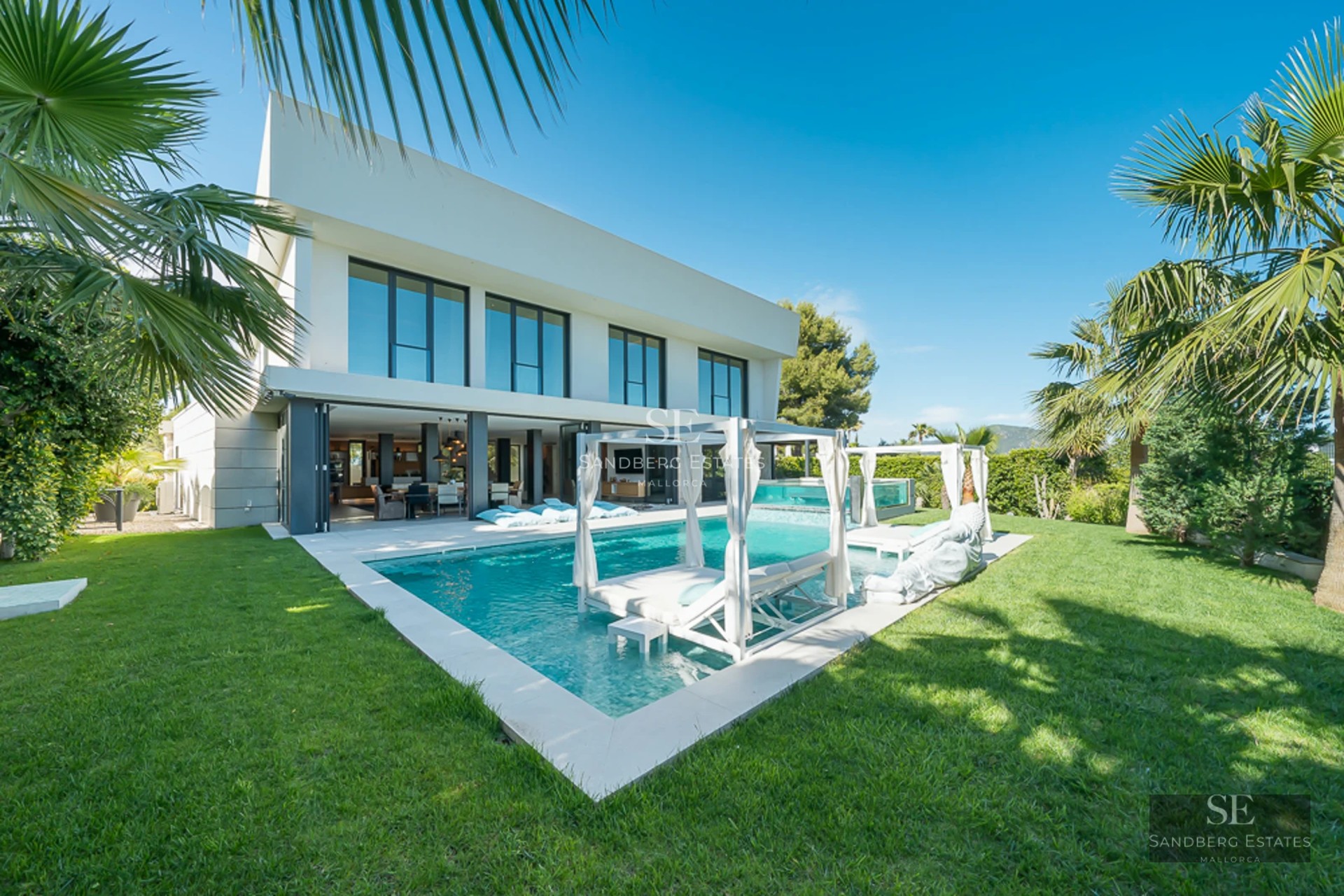 View of turquoise pool surrounded by lush greenery and modern architecture. White lounge chairs and umbrellas invite relaxation.