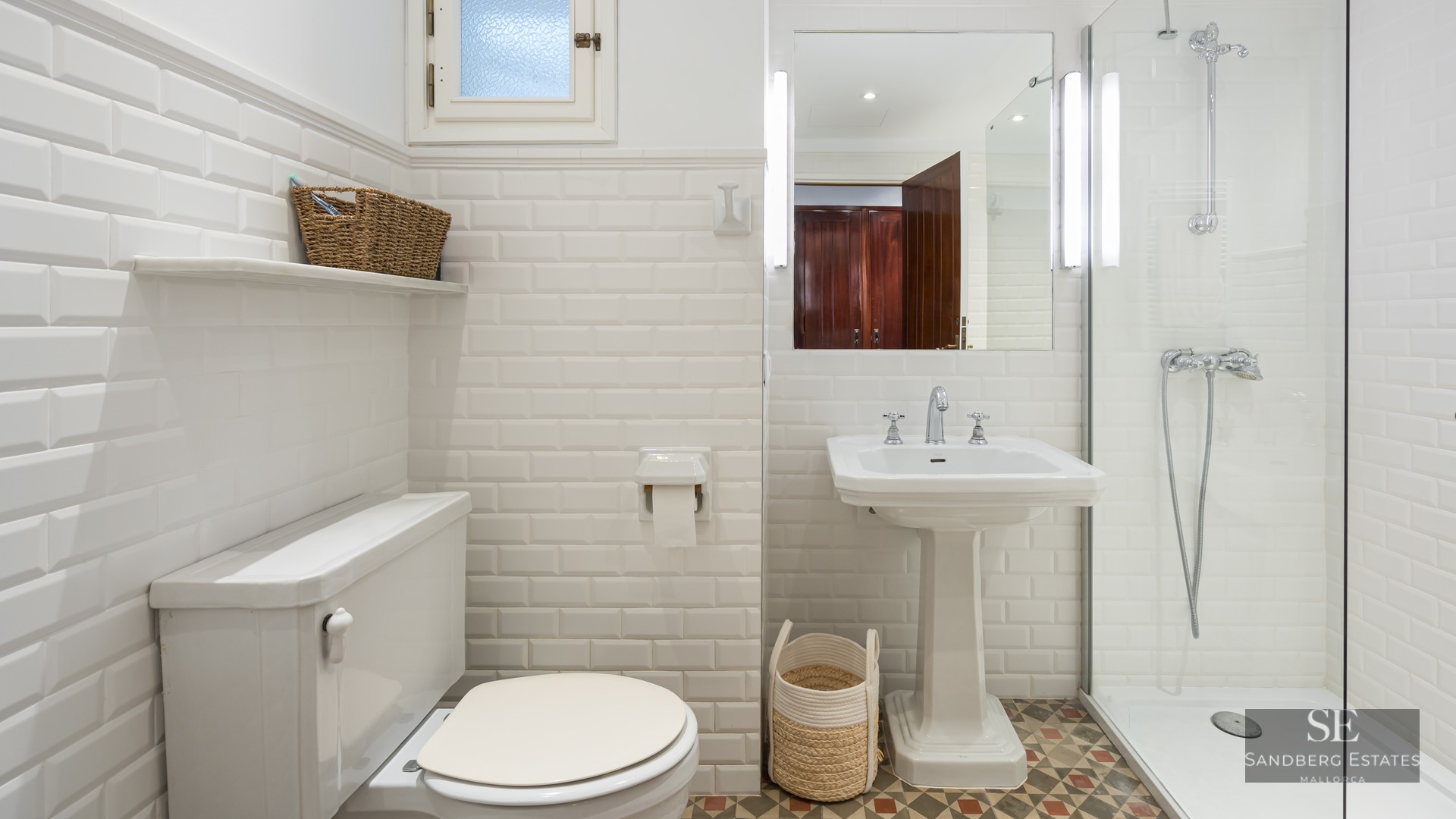 Bright bathroom with white subway tiles, pedestal sink, glass shower, and patterned floor tiles.