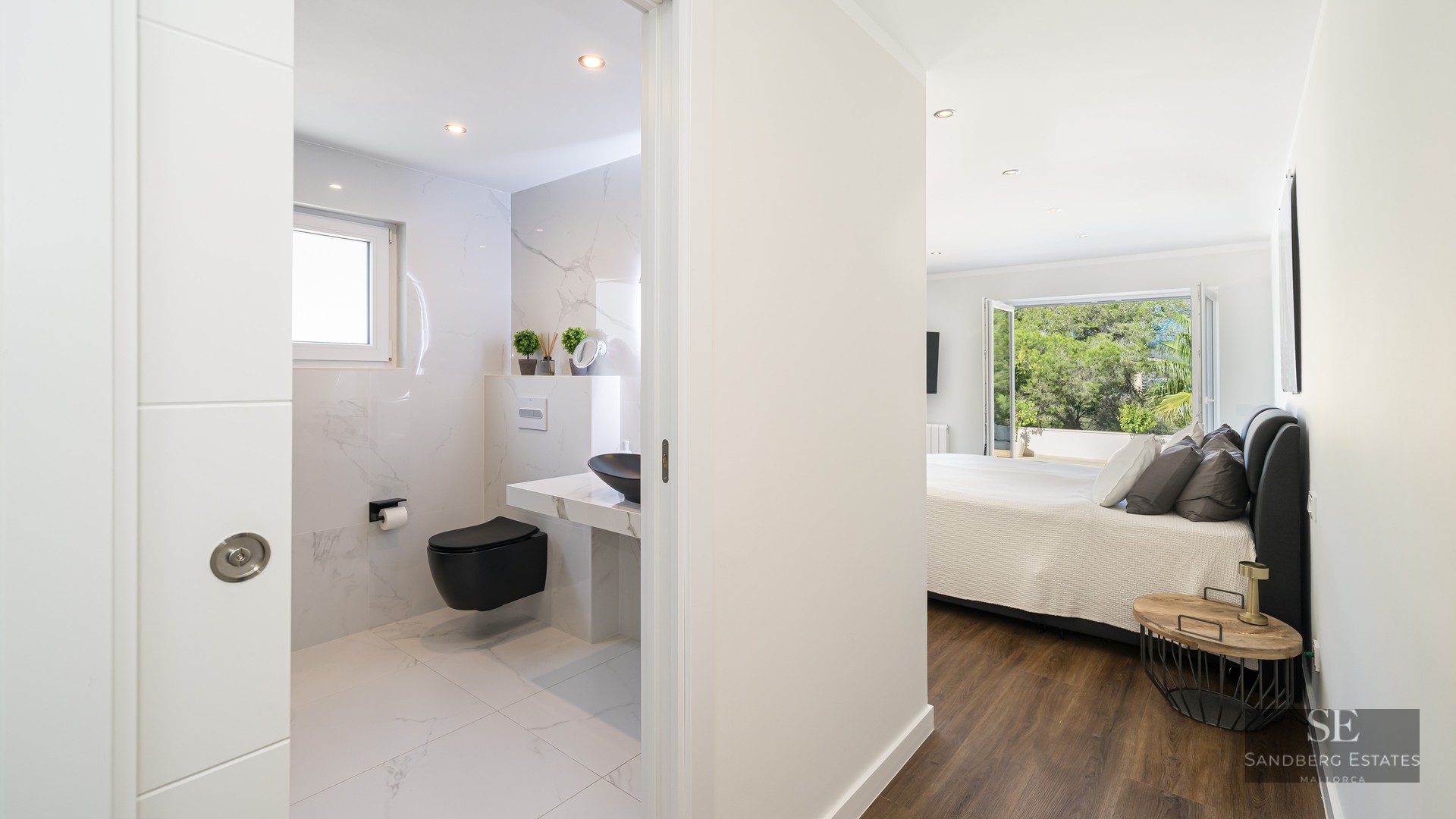 Chambre parentale lumineuse avec parquet et salle de bain moderne en marbre blanc et noir.