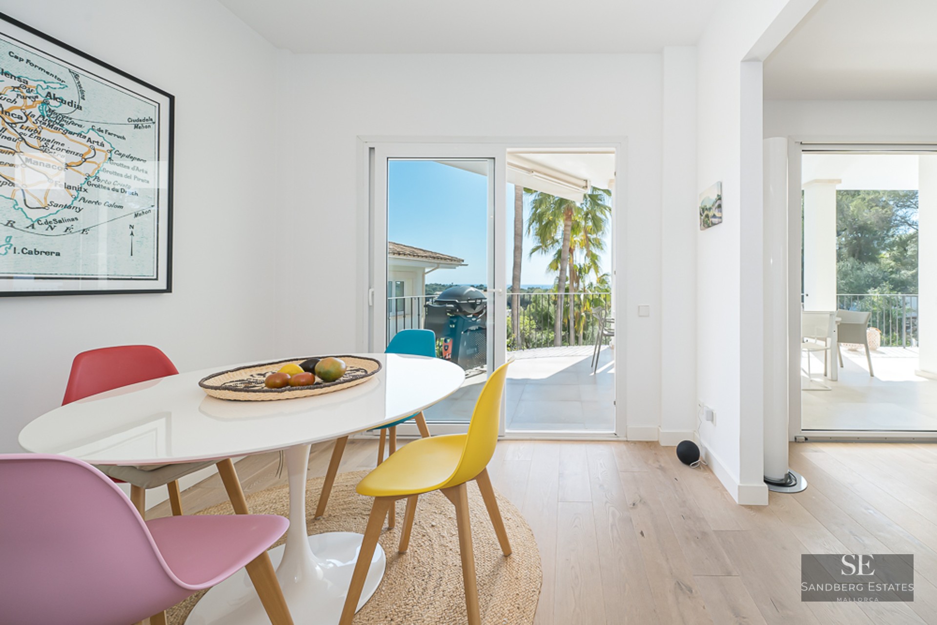 Salle à manger moderne avec table blanche et chaises colorées près de baies vitrées donnant sur une terrasse.