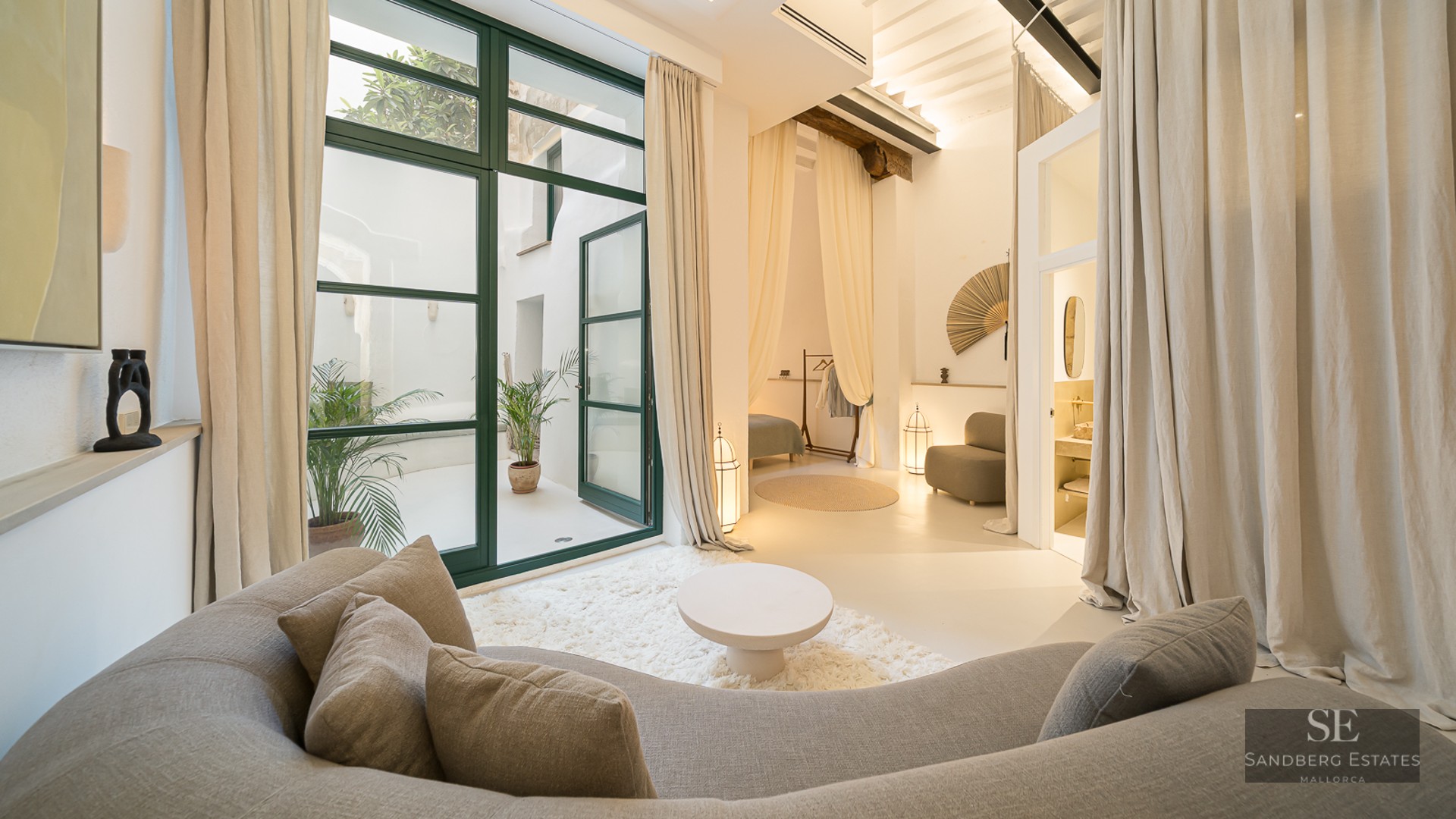 Salon moderne avec un canapé gris incurvé, un tapis à poils longs et de grandes portes vitrées ouvrant sur un patio.