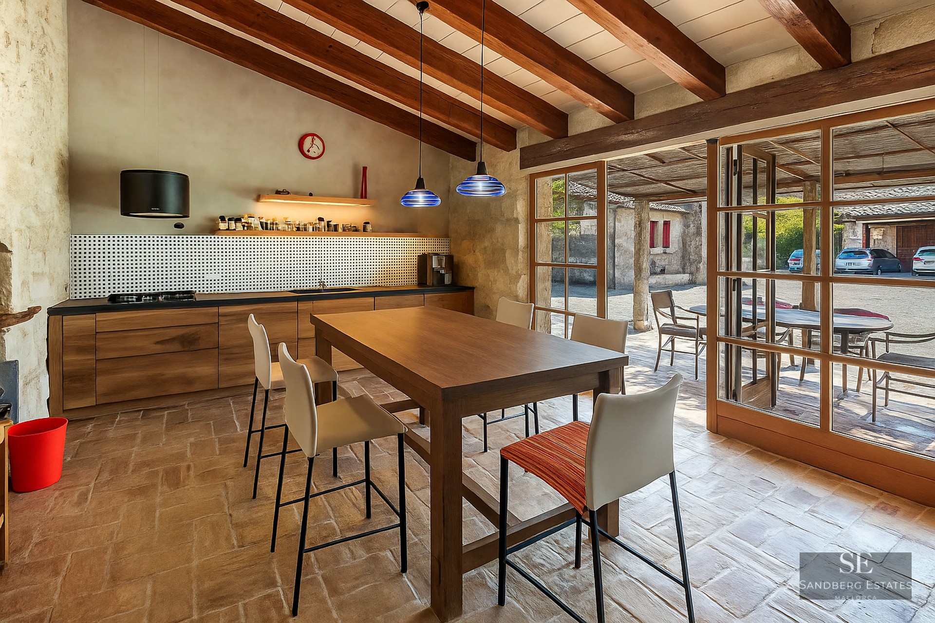 Kitchen with wooden beams, terracotta flooring, and large glass doors leading to an outdoor courtyard.