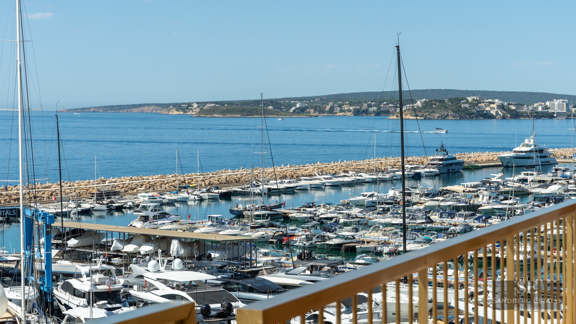 Panoramic view of a luxury marina with yachts and the blue Mediterranean sea from a terrace.