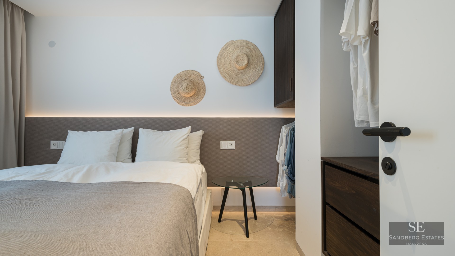 Modern bedroom featuring a backlit headboard, white linens, and decorative straw hats on the wall.