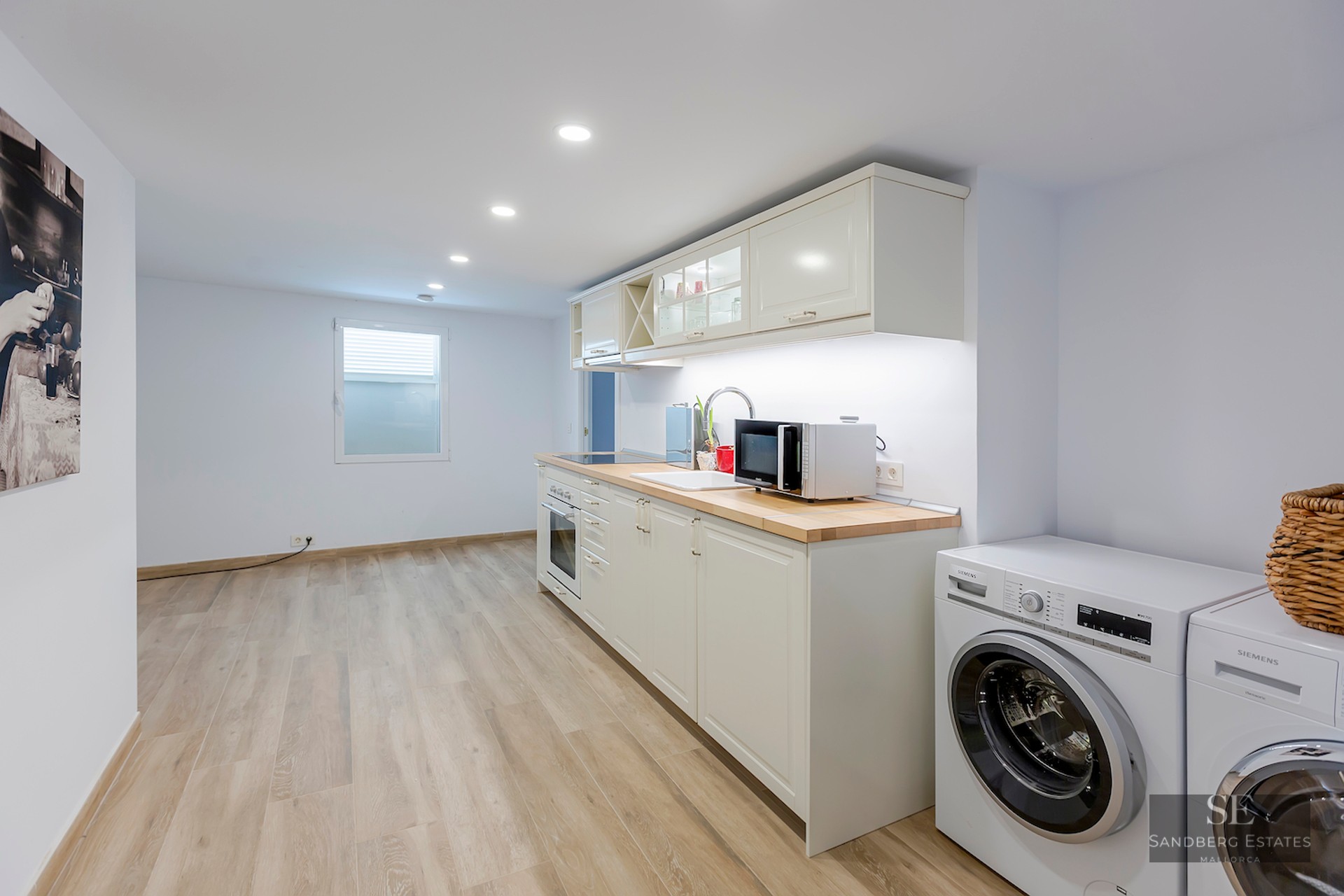 Bright modern kitchen with white cabinets, light wood countertops, and integrated washing machine and dryer.