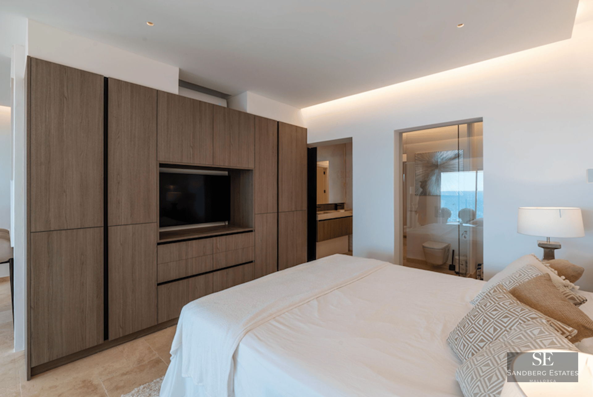 Modern bedroom featuring a large wood closet with integrated TV and a glass-walled ensuite bathroom with sea view.