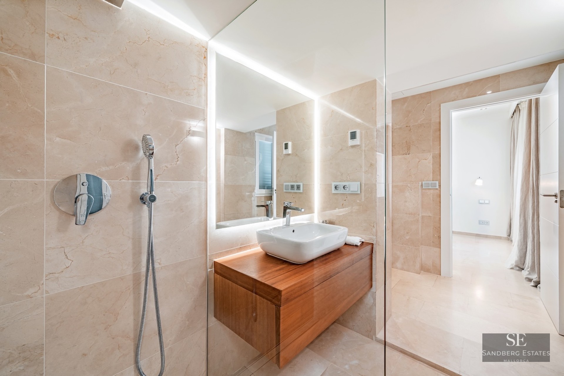 Modern bathroom featuring beige marble walls, a glass walk-in shower, and a floating wood vanity with a white vessel sink.