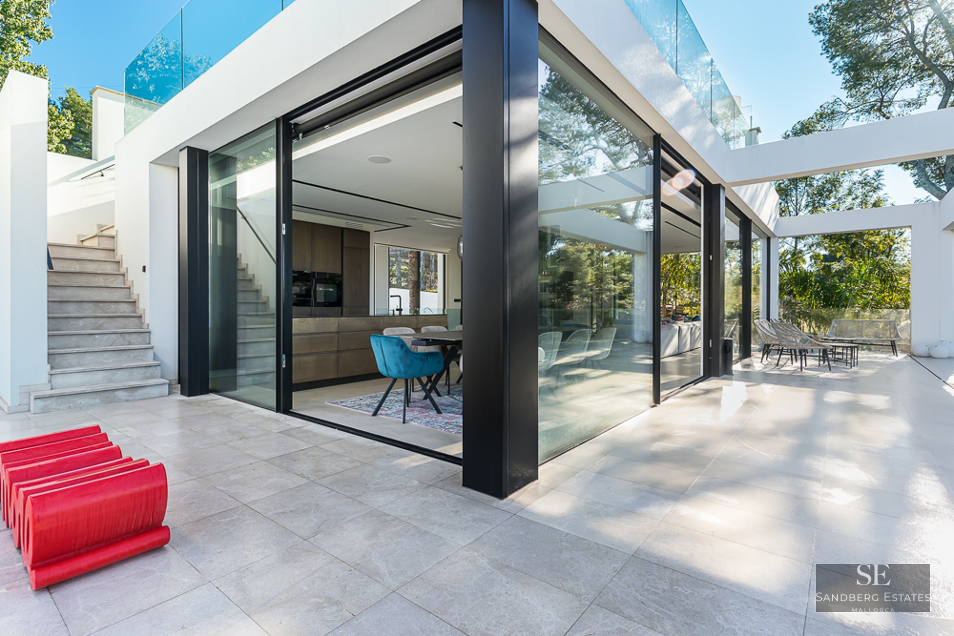 Luxury terrace with large floor-to-ceiling glass windows, light stone flooring, and a view into a modern interior kitchen.