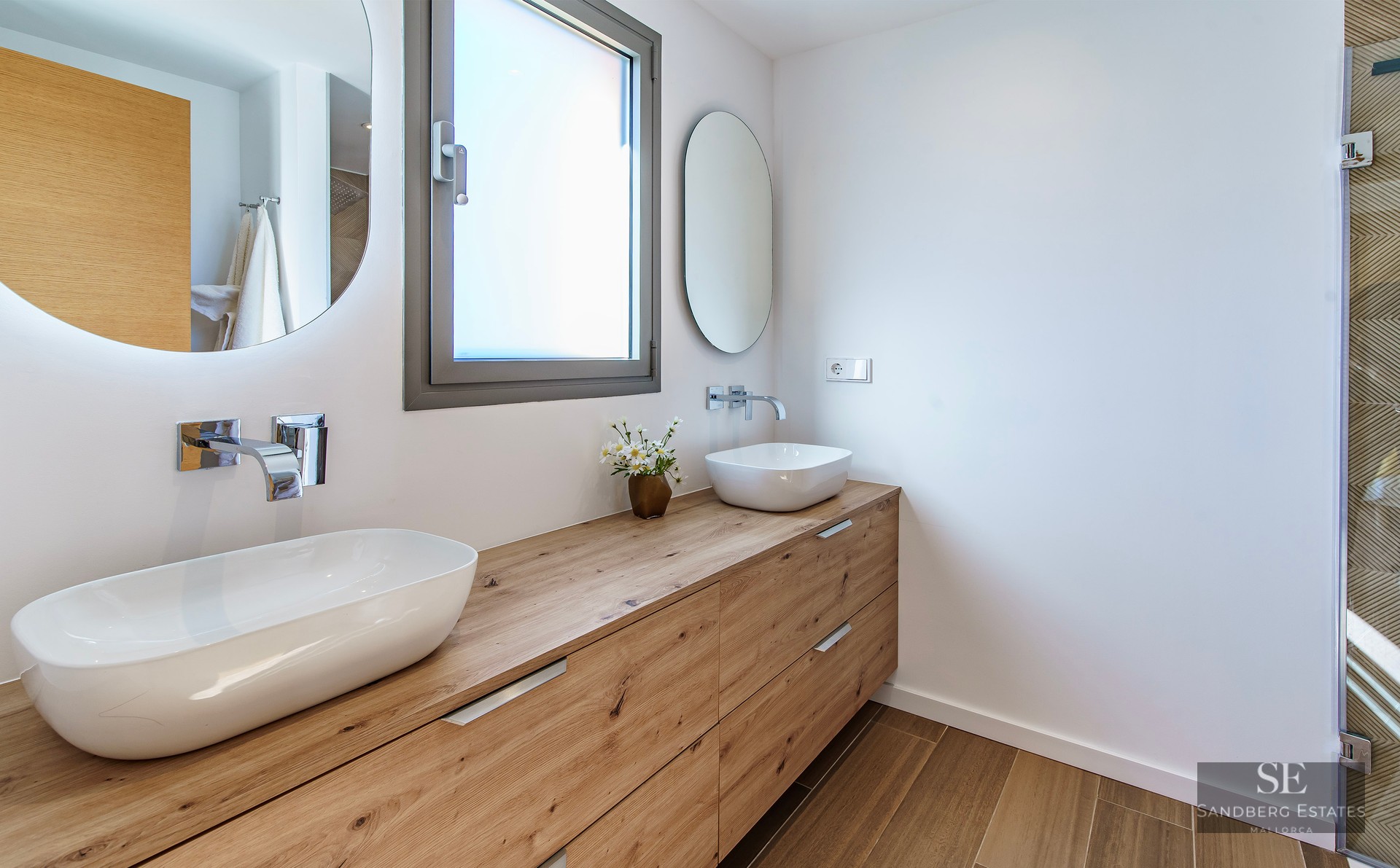Modern bathroom featuring a long wooden vanity with two white vessel sinks and backlit circular mirrors.