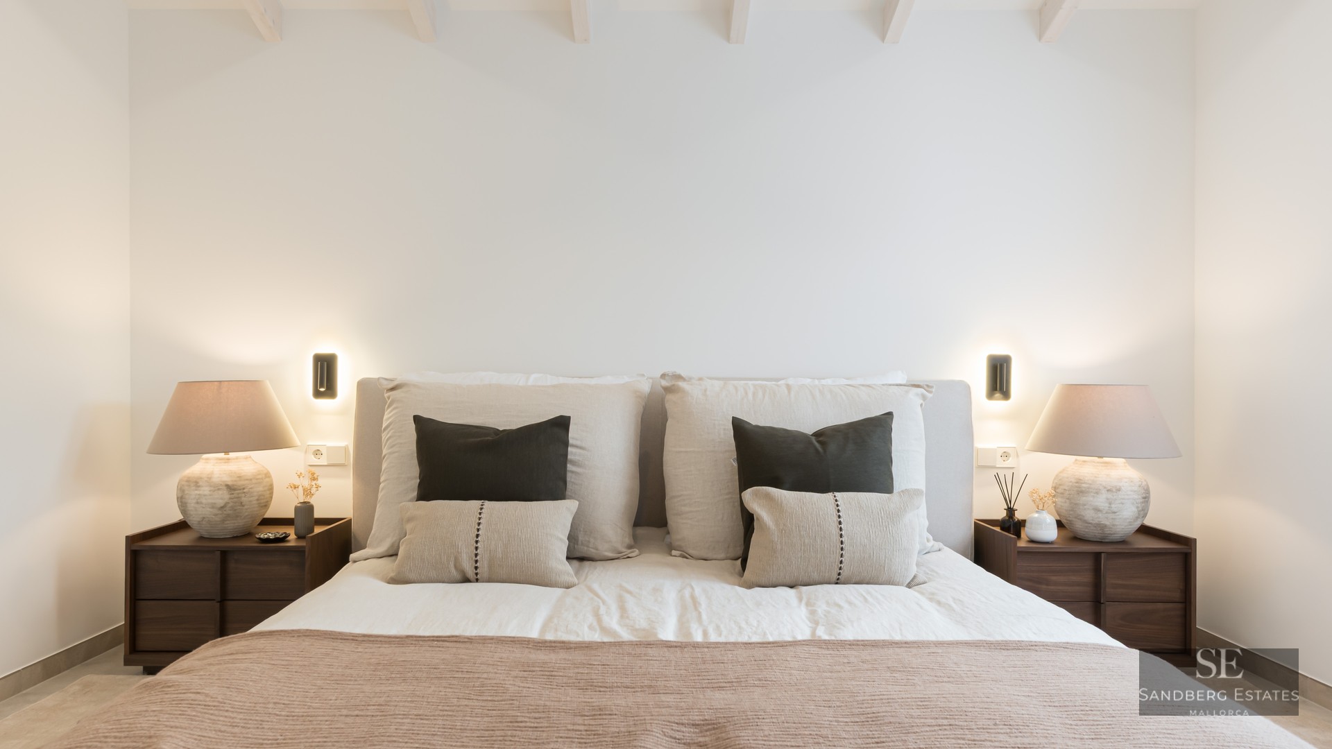 Bed with padded headboard, decorative pillows, wooden nightstands, and designer lamps with warm ambient light.