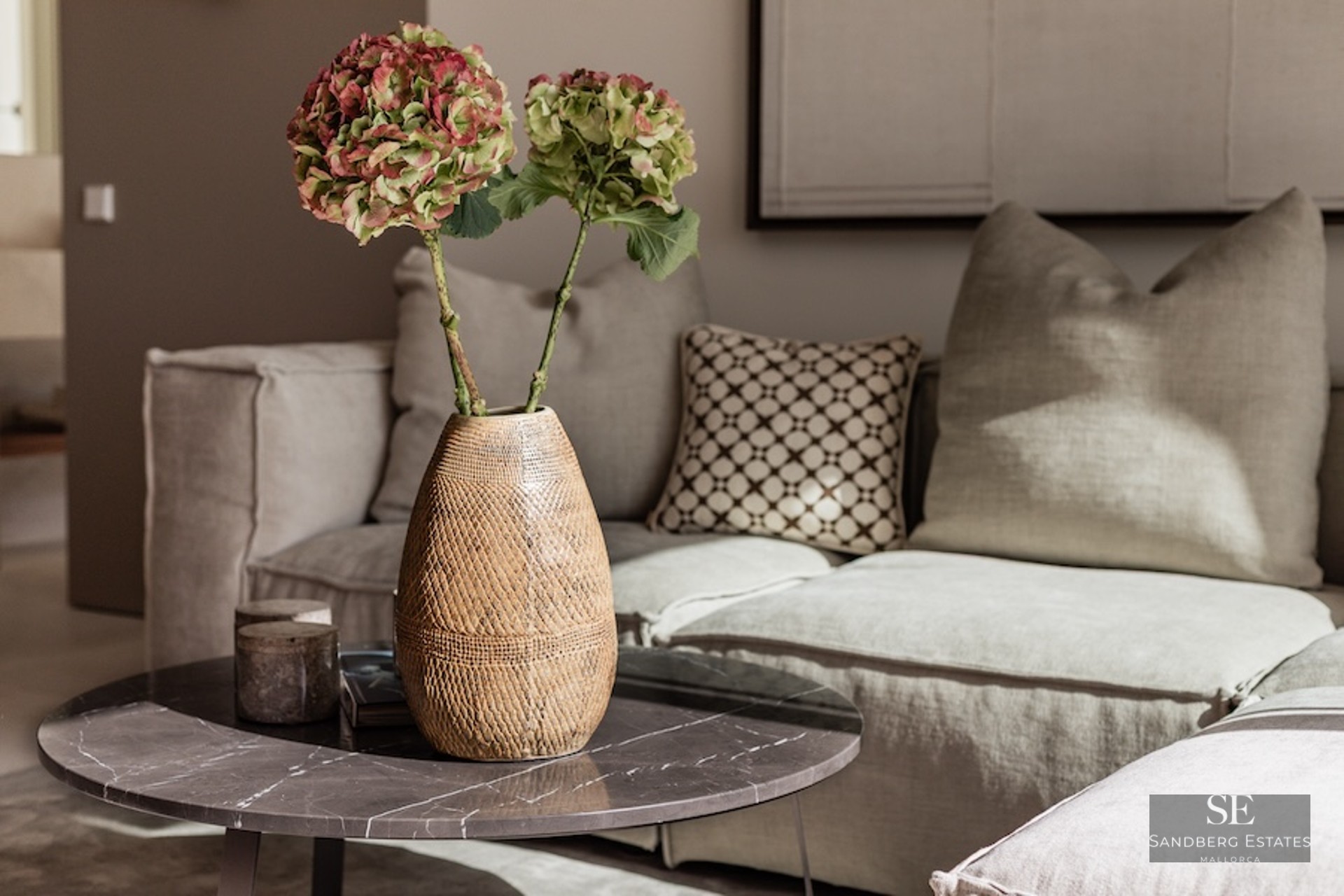 Close-up of a marble coffee table with a ceramic vase of flowers in front of a neutral linen sofa.