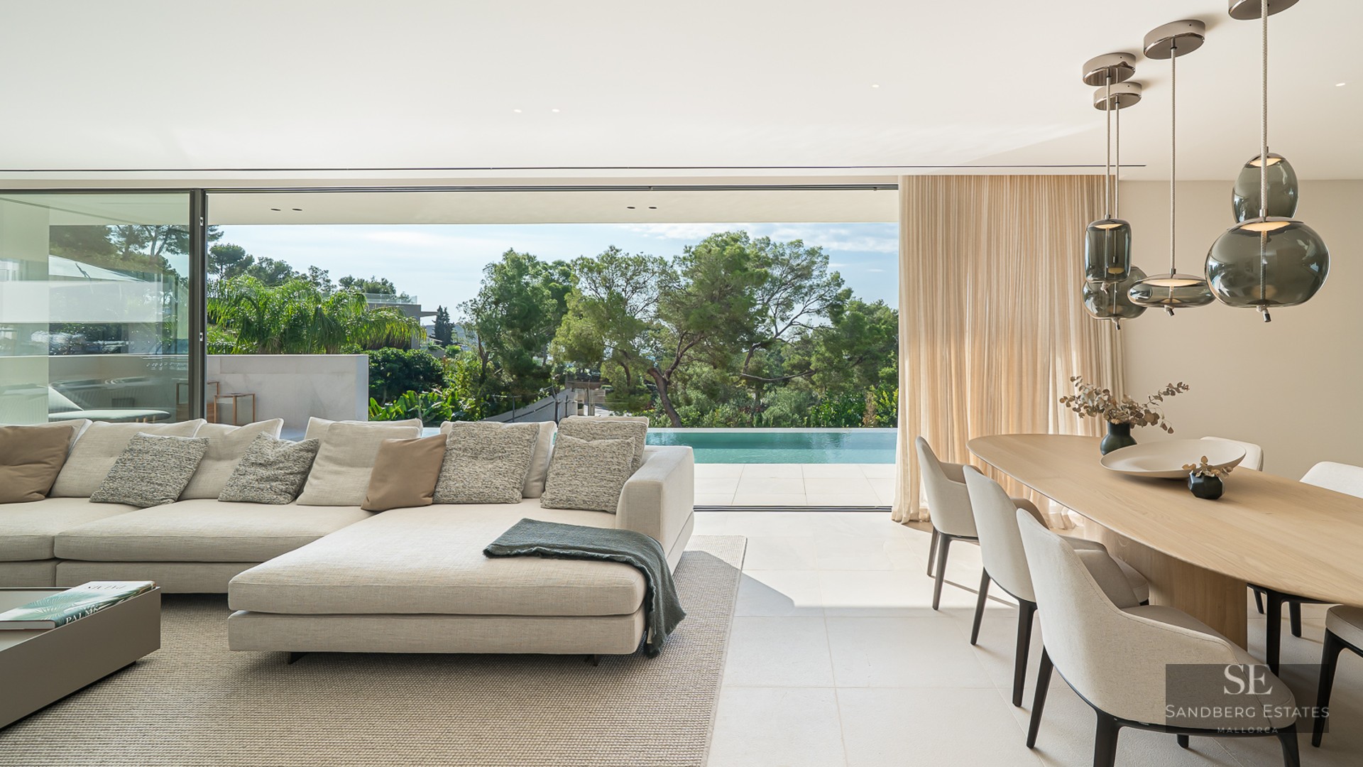 Elegant modern living room featuring a beige sectional, dining set, and large sliding doors opening to a pool terrace.