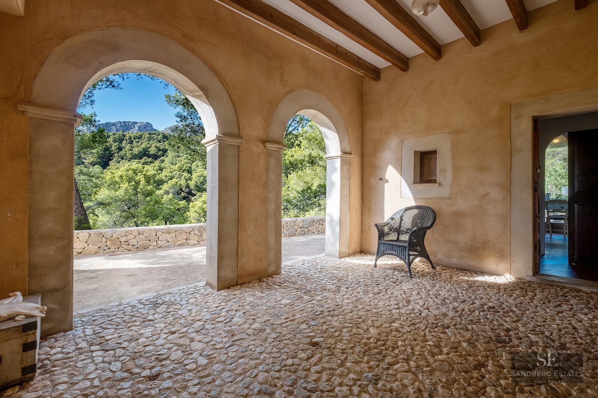 Rustic terrace featuring stone arches, wooden beams, cobblestone flooring, and a scenic mountain forest view.