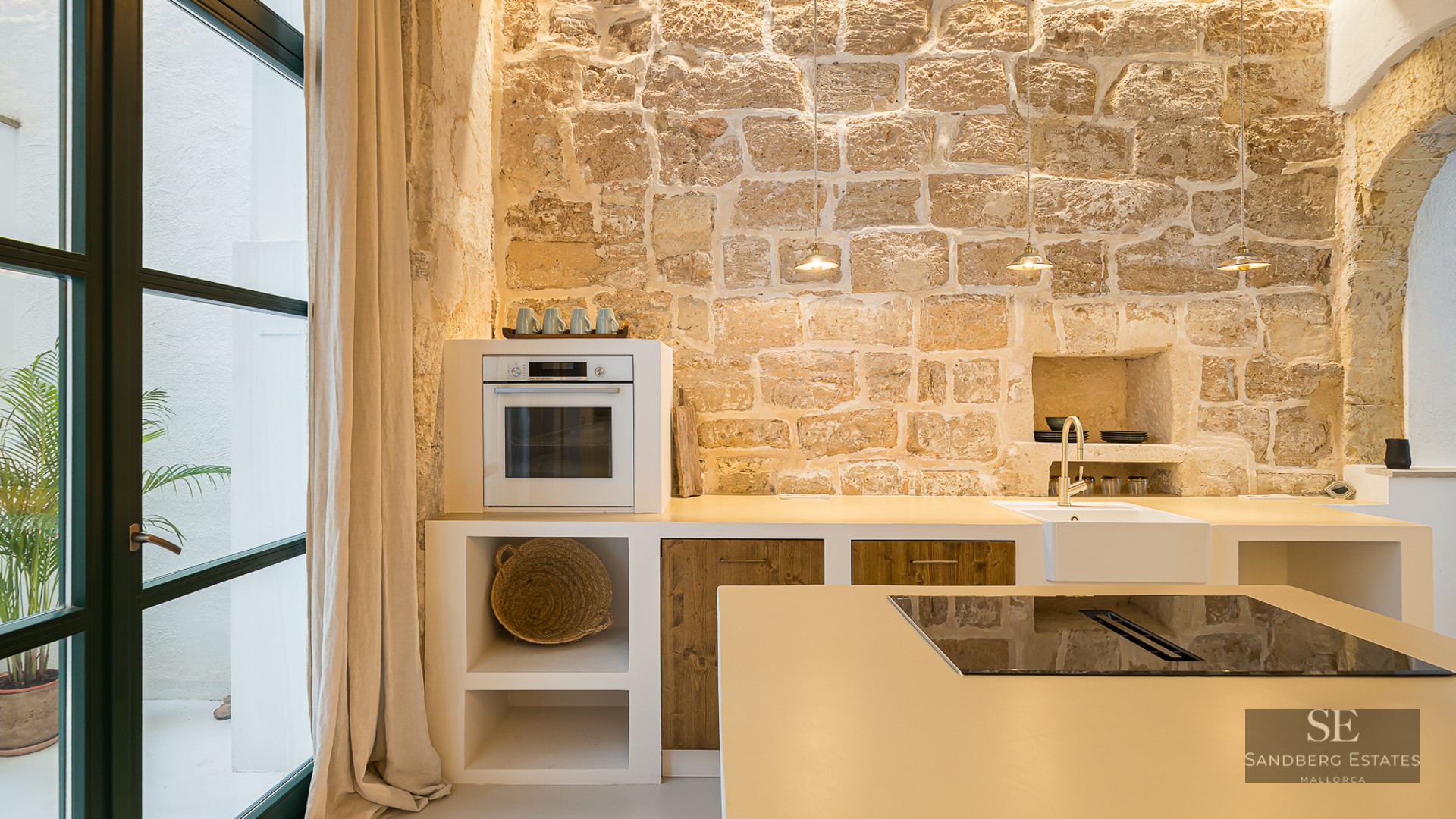 A modern kitchen featuring a large rustic stone wall, white countertops, wooden cabinets, and a large glass door.
