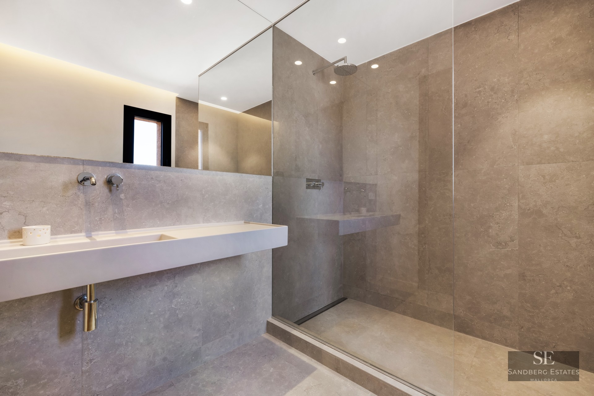 Minimalist bathroom with gray stone tiles, glass walk-in shower, wall-mounted sink, and large mirror.