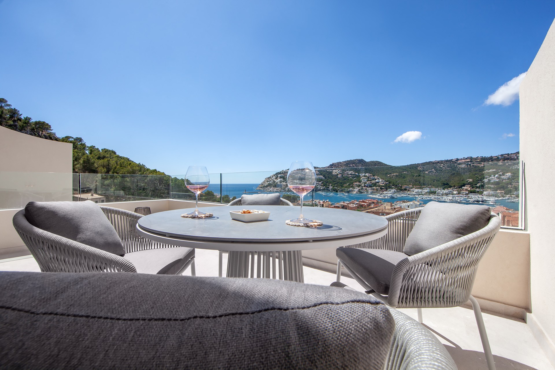 Table de terrasse moderne avec deux verres de vin devant une vue imprenable sur le port et la mer par temps clair.