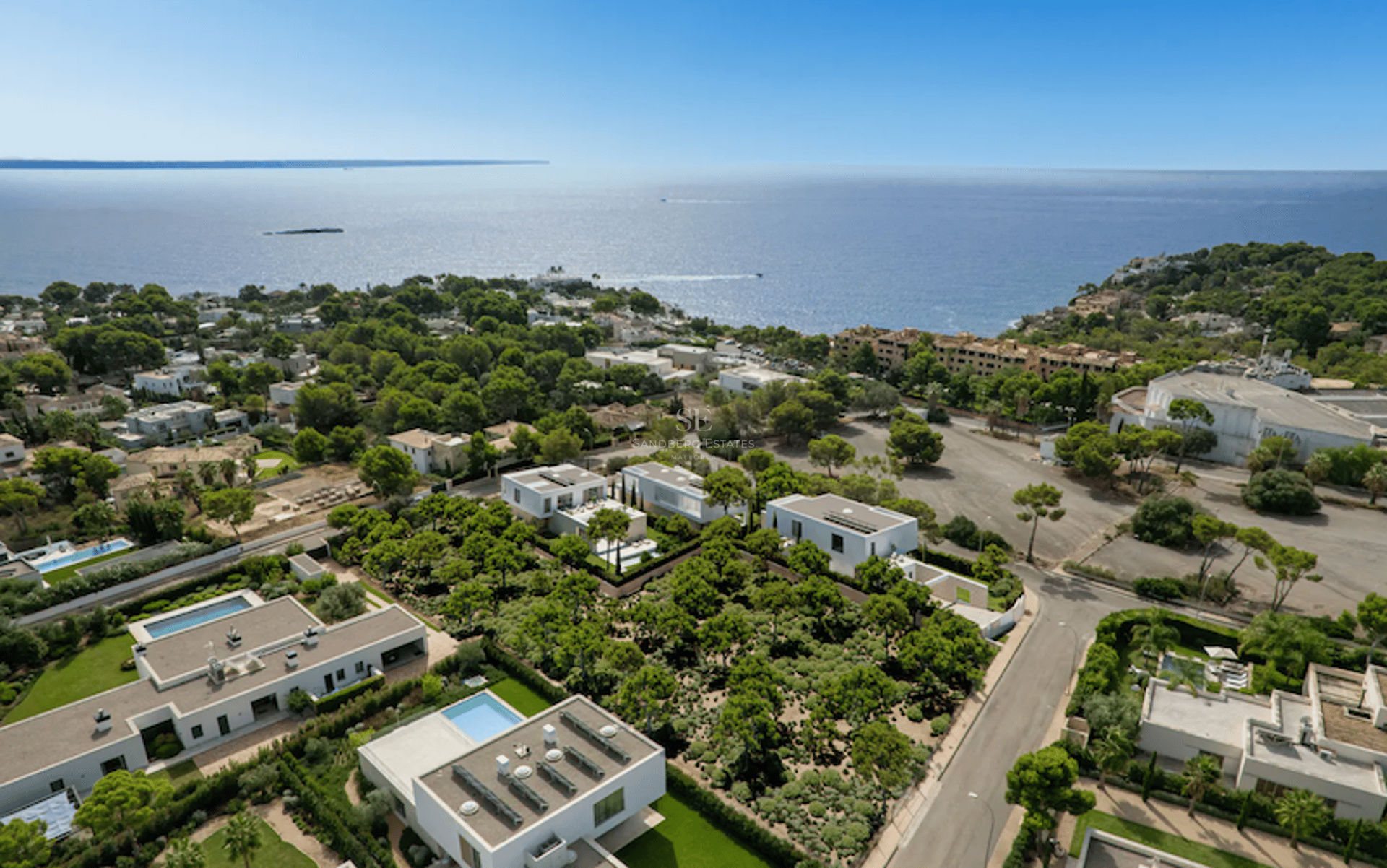 Vue aérienne de villas blanches modernes entourées de pins avec la mer Méditerranée à l'horizon.