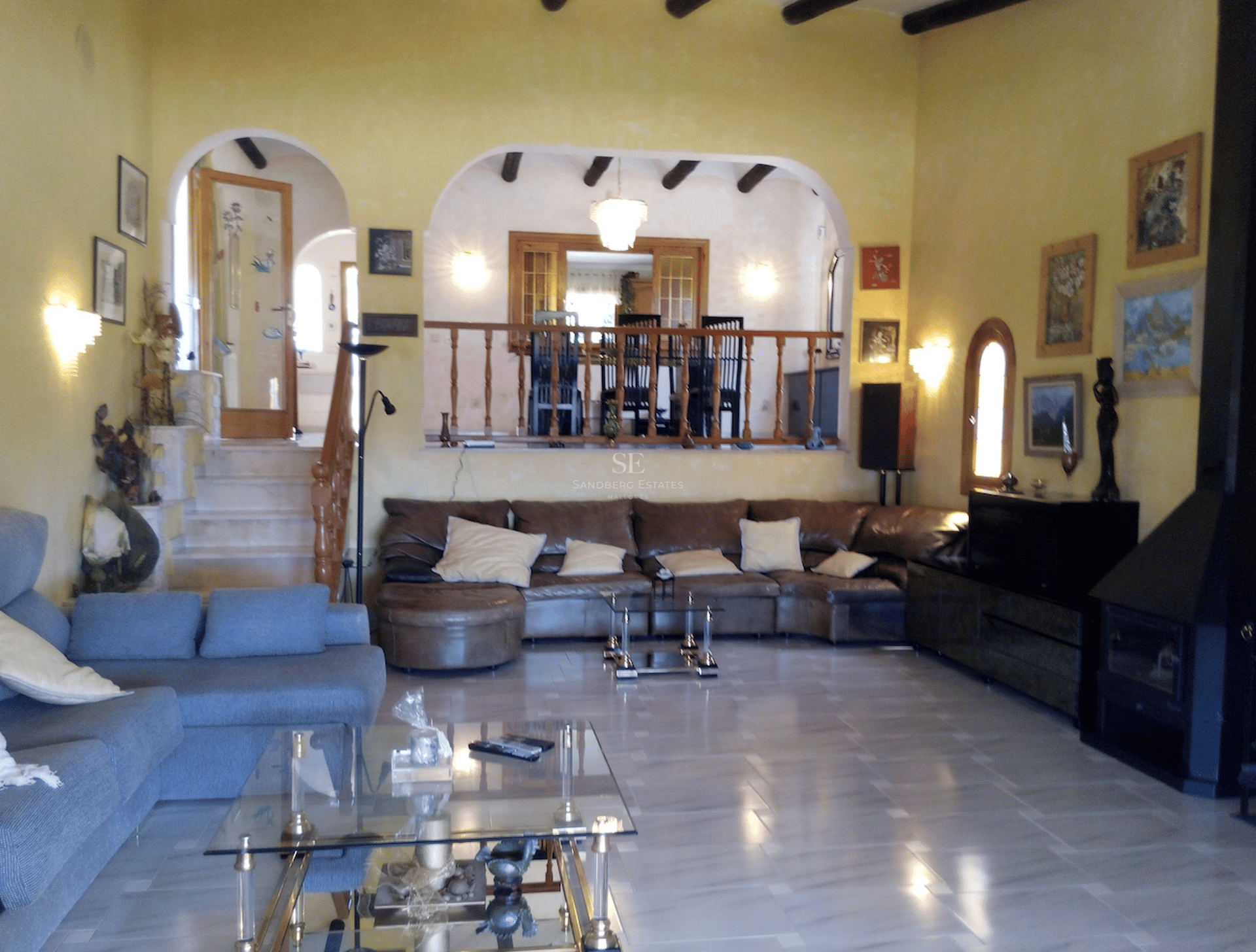 Amplio salón con suelos de mármol pulido, techos con vigas de madera, arcos decorativos y zona de comedor elevada.