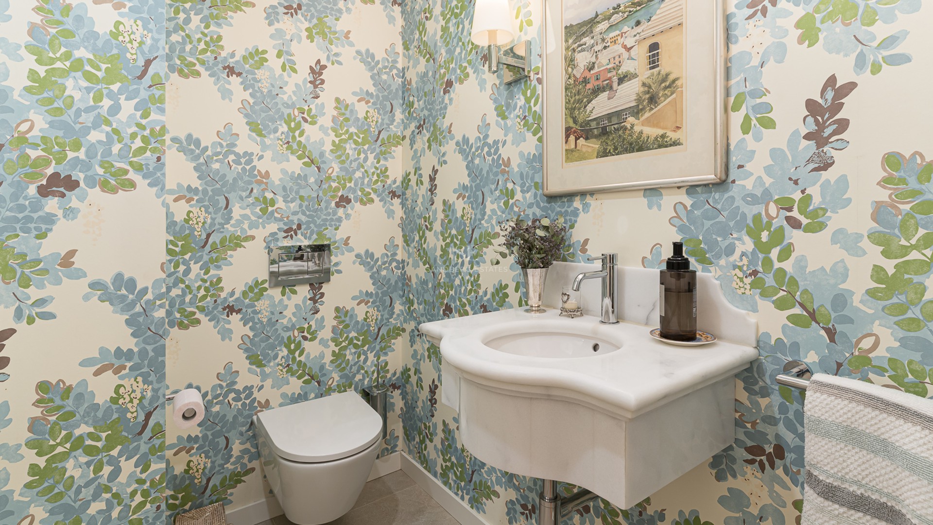 Guest bathroom featuring floral wallpaper, a sculpted marble washbasin, and a wall-mounted toilet.