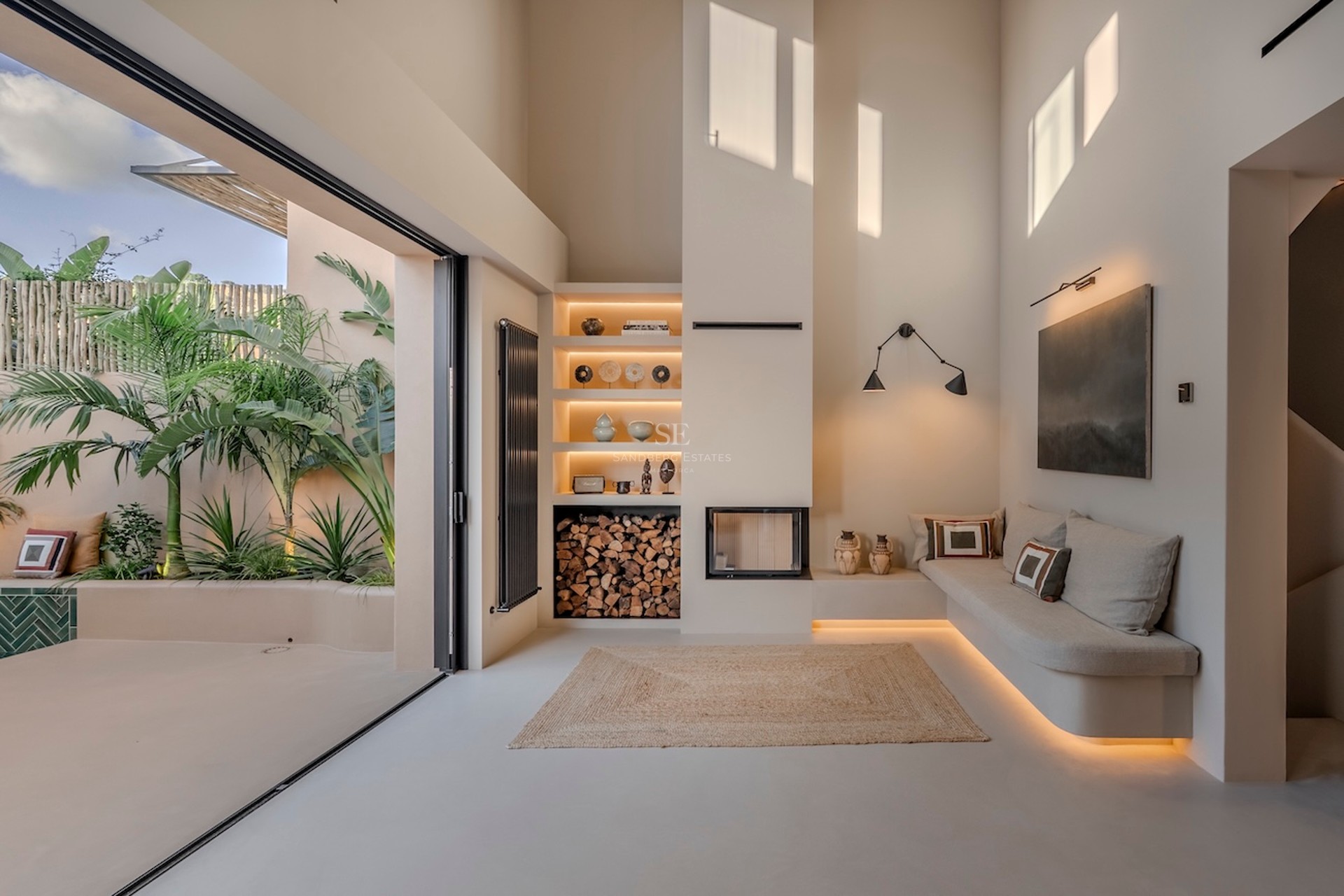 Salon épuré avec cheminée intégrée, banquette sur mesure et grandes baies vitrées donnant sur un jardin tropical.