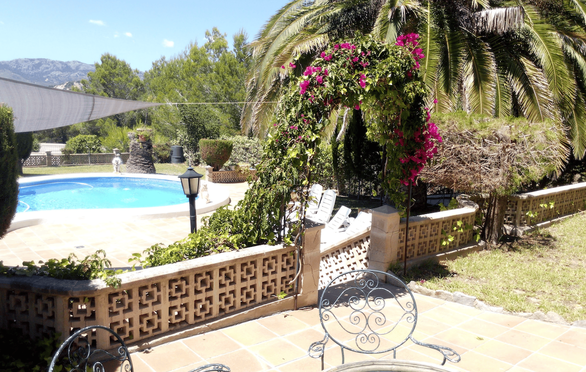 Terraza soleada con piscina circular, baldosas de terracota, un arco de buganvillas y montañas al fondo.