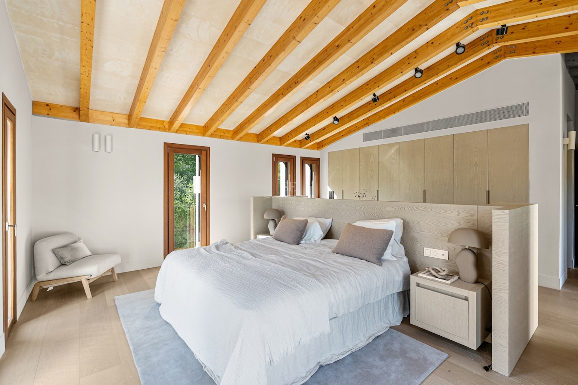 Chambre principale moderne avec plafond incliné, poutres en bois, grand lit et placards intégrés.