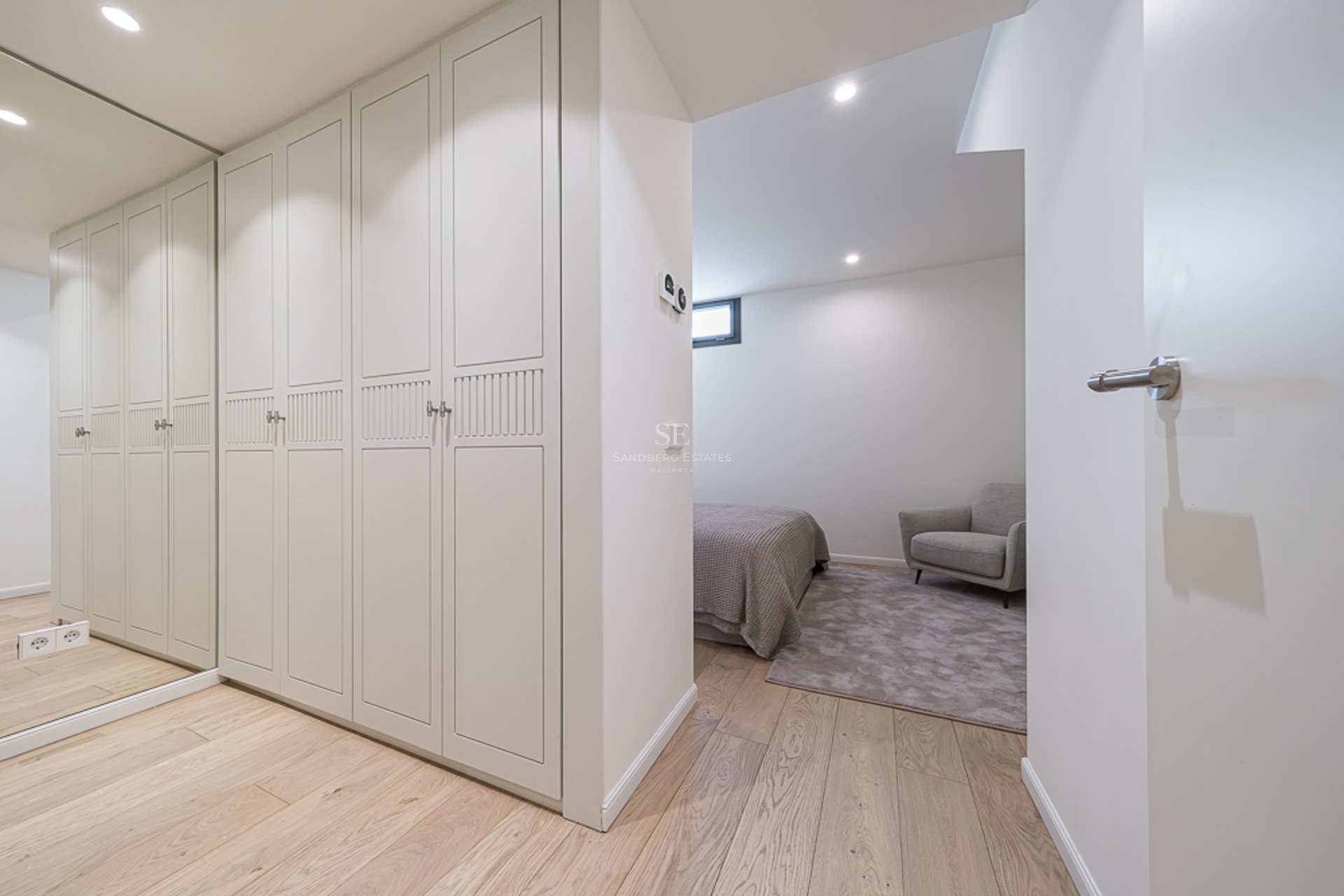 Modern bedroom view showing white built-in wardrobes, a full-length mirror, and light oak floors.